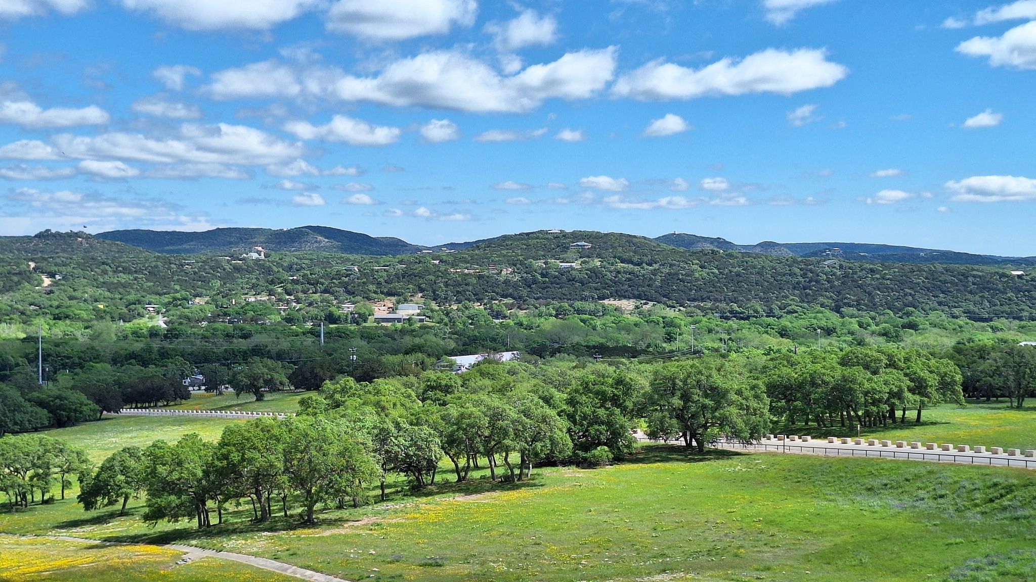 Sunny landscape with green rolling hills, lush trees, and open grassy fields. - Dam Crest Trail