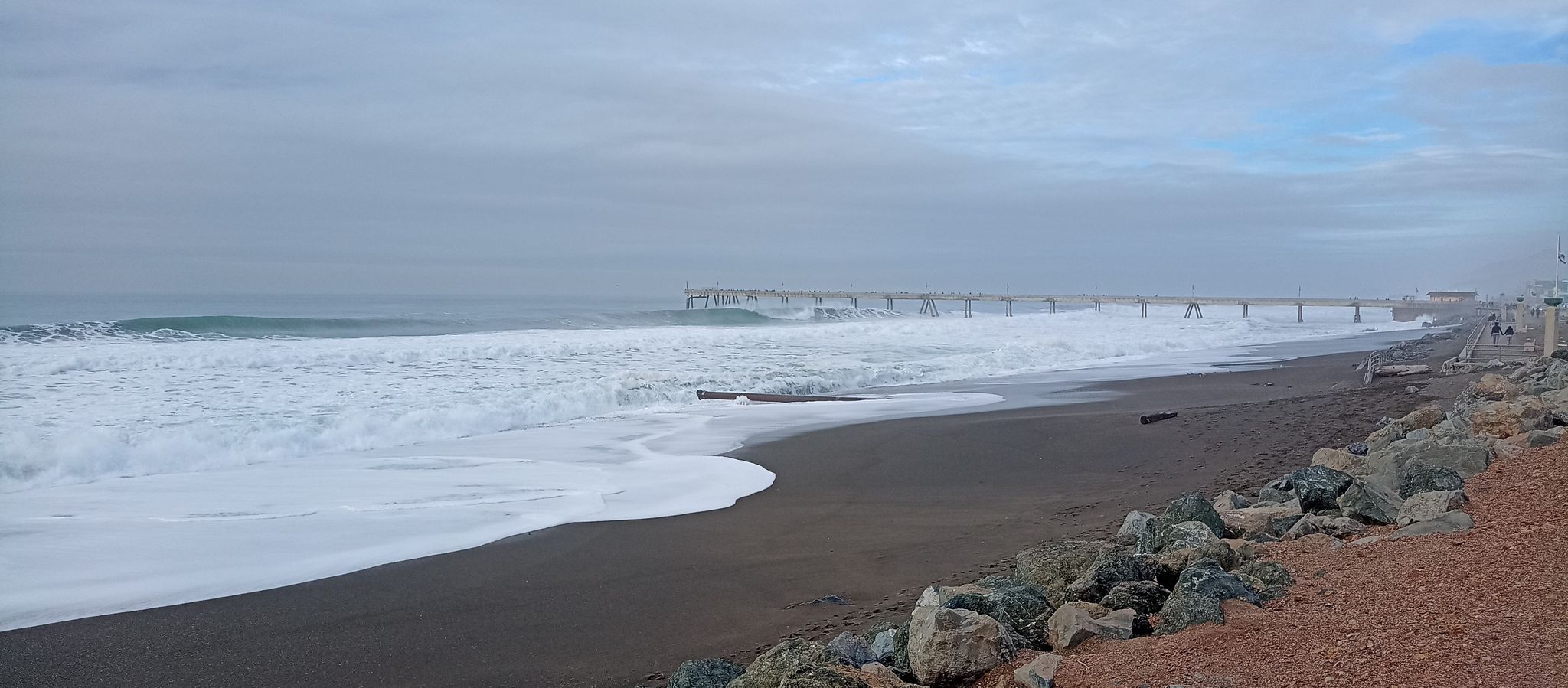Overcast view of a wide sandy beach, large ocean waves, and a distant pier. - Pacifica Pier – Sharp Park Beach loop from Mussel Rock