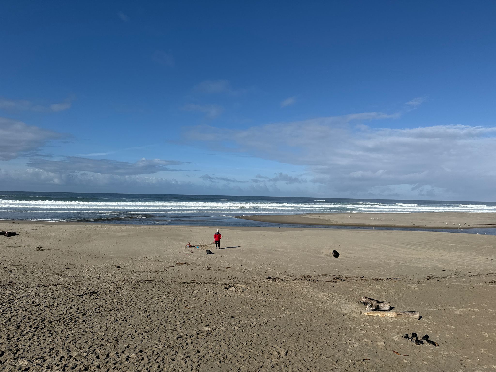 A person in red walks on a wide sandy beach by the ocean. - South Lincoln City loop