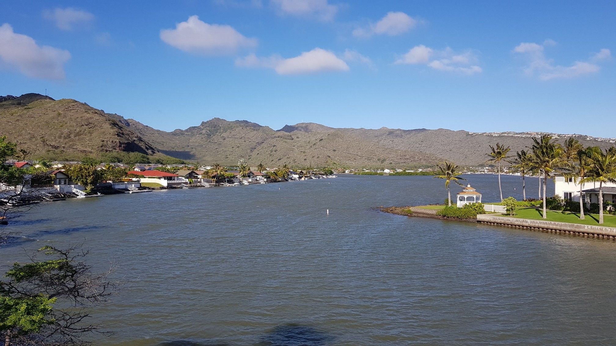 Calm bay with distant mountains, houses, and palm trees under blue sky. - Kahala to Makapu‘u Head via East Honalulu