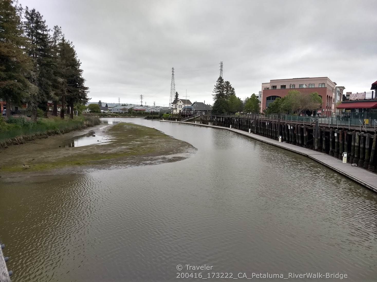 A wide river with a wooden boardwalk and buildings under a cloudy sky. - Bay Area Ridge Trail: Lynch Creek Trail