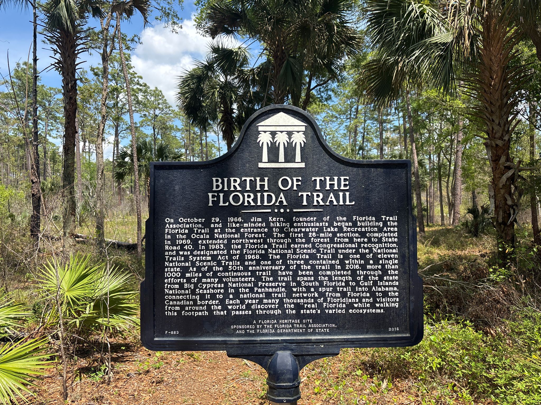A black historical marker sign stands in a sunny forest clearing. - Hiking loop from Paisley