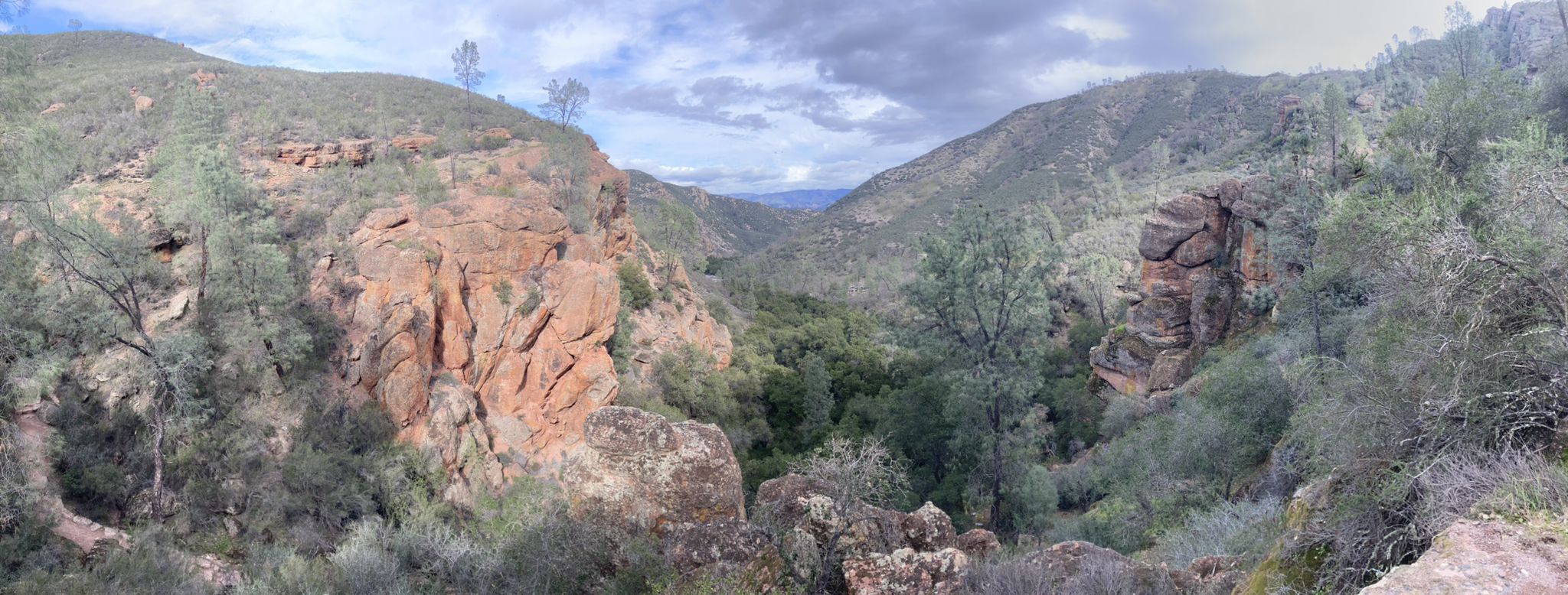Panoramic view of a valley with rocky hillsides and green trees under a cloudy sky. - Moses Spring and Rim Trail Loop