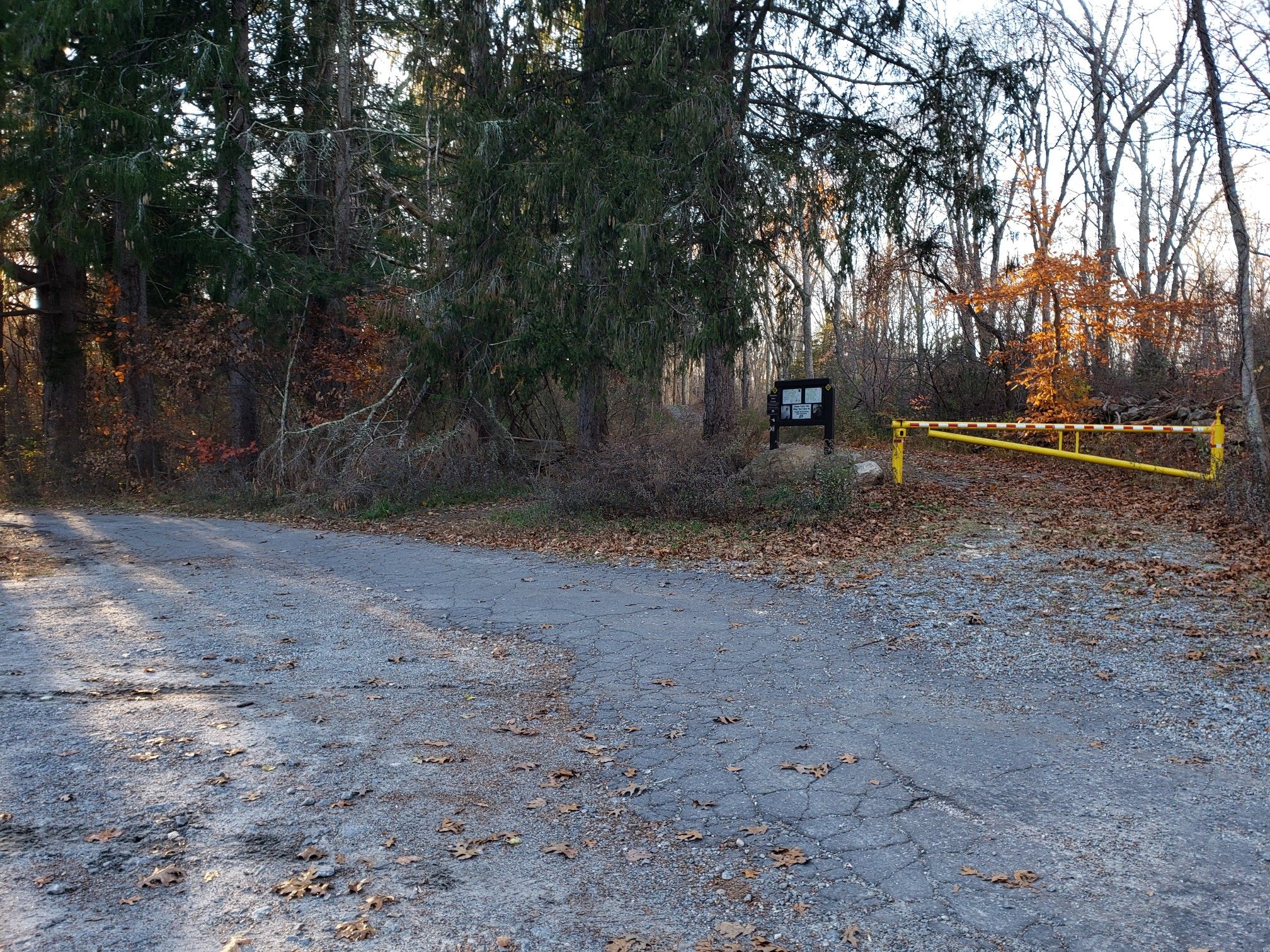 A dirt parking area with a yellow gate and sign at a forest edge. - Richard H. Goodwin Trail