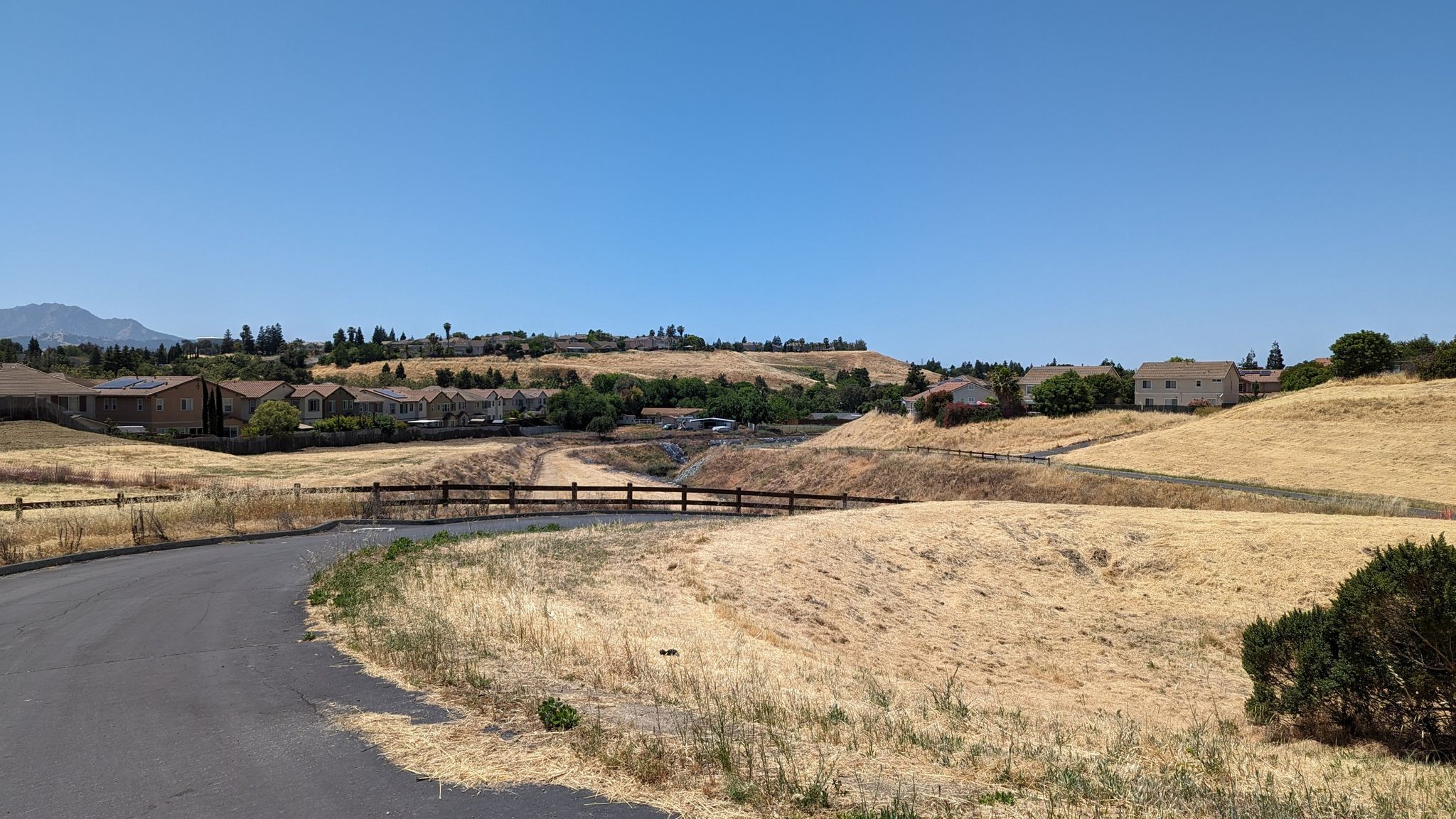 Paved road winding through dry golden hills with distant houses under clear sky. - Delta de Anza, Mokelumne & Marsh Creek Trails Loop