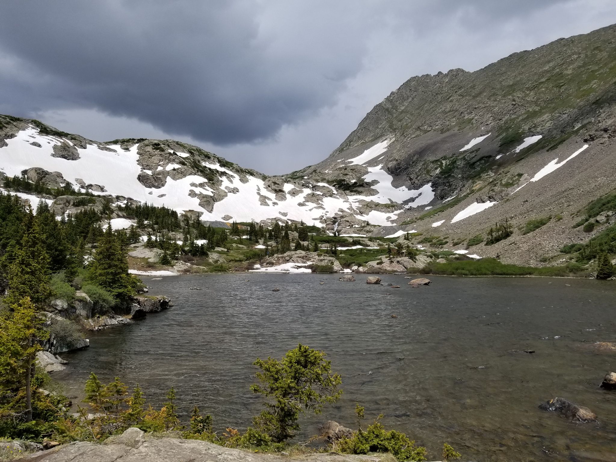 Dark mountain lake with snow patches on surrounding peaks under cloudy sky. - Spruce Creek Trail to Mohawk Lakes Trail