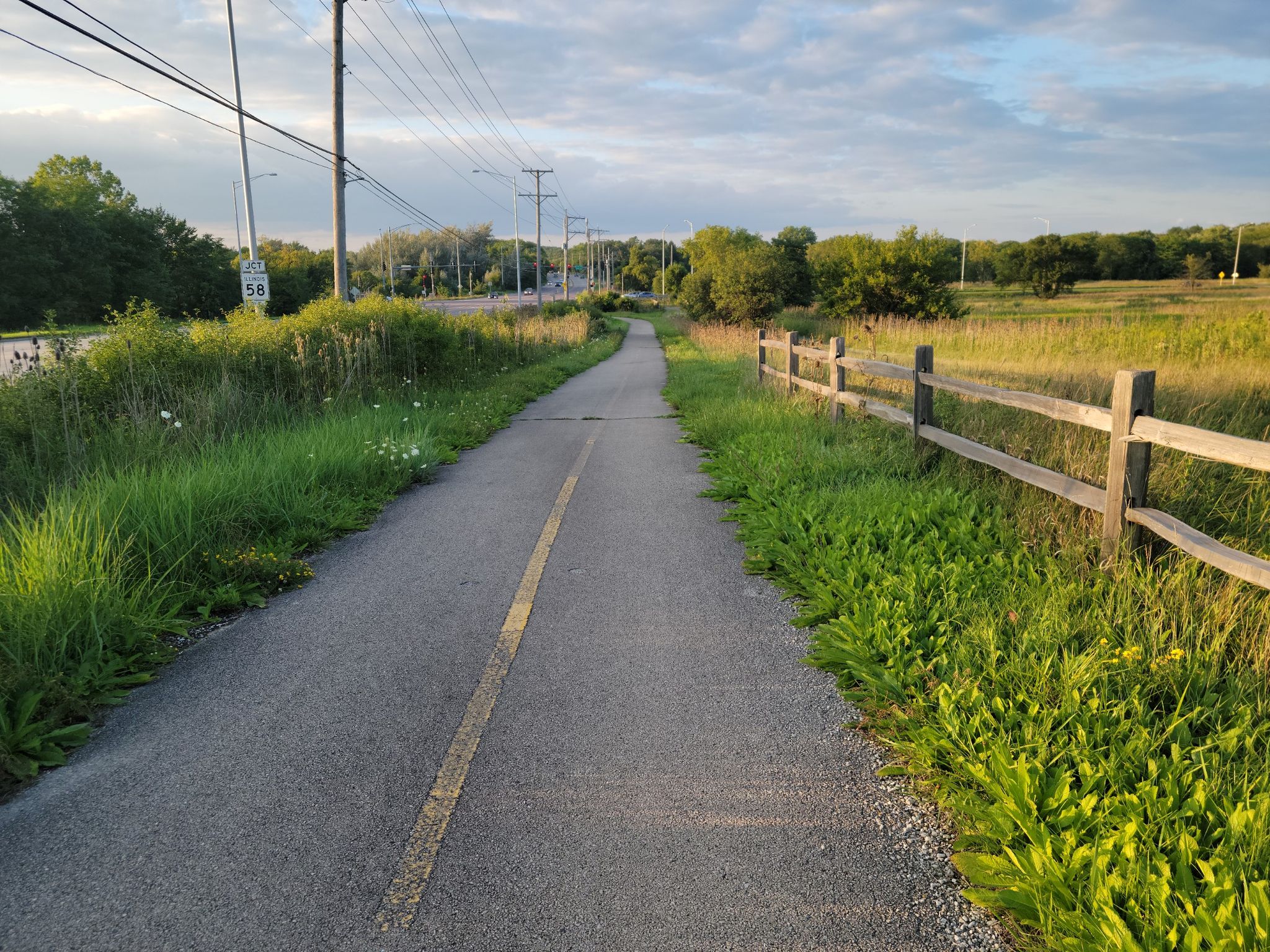 Paved path next to a wooden fence and grassy field at sunset. - Poplar Creek, Spring Lake & Paul Douglas Preserve loop