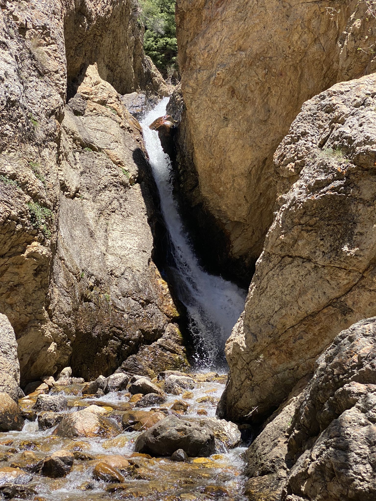 A powerful waterfall plunges between towering rock formations into a rocky stream. - Hidden Falls Trail