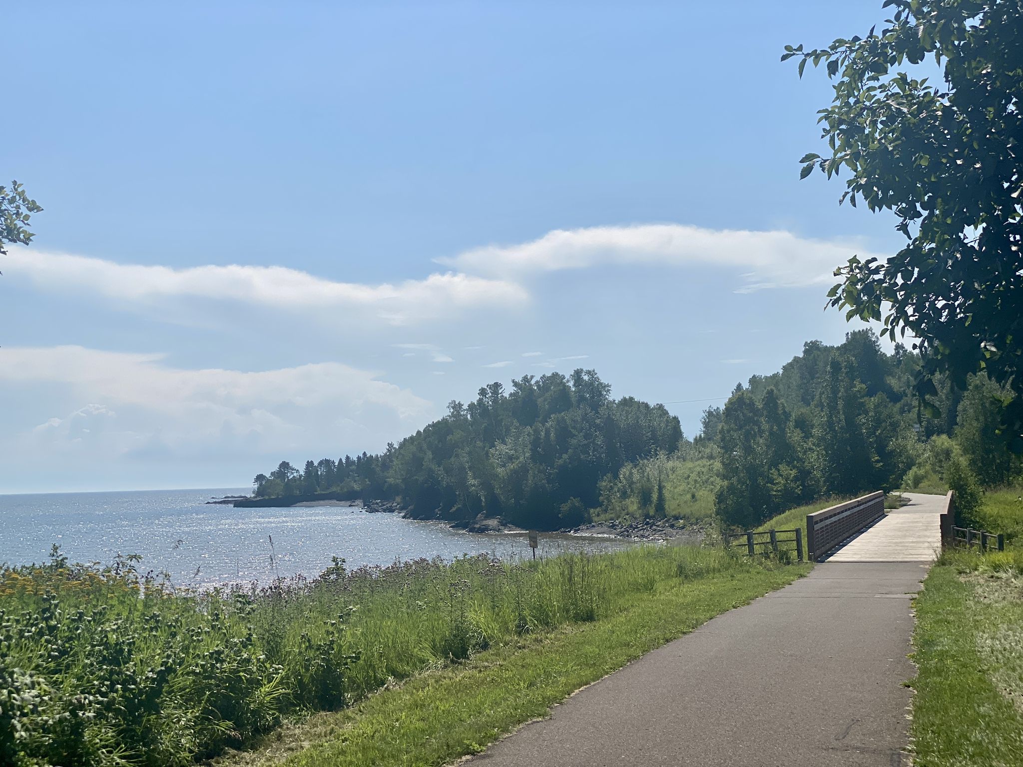 A paved path leads to a bridge beside a calm lake and lush green shoreline. - Beaver River – Split Rock River loop from Silver Bay