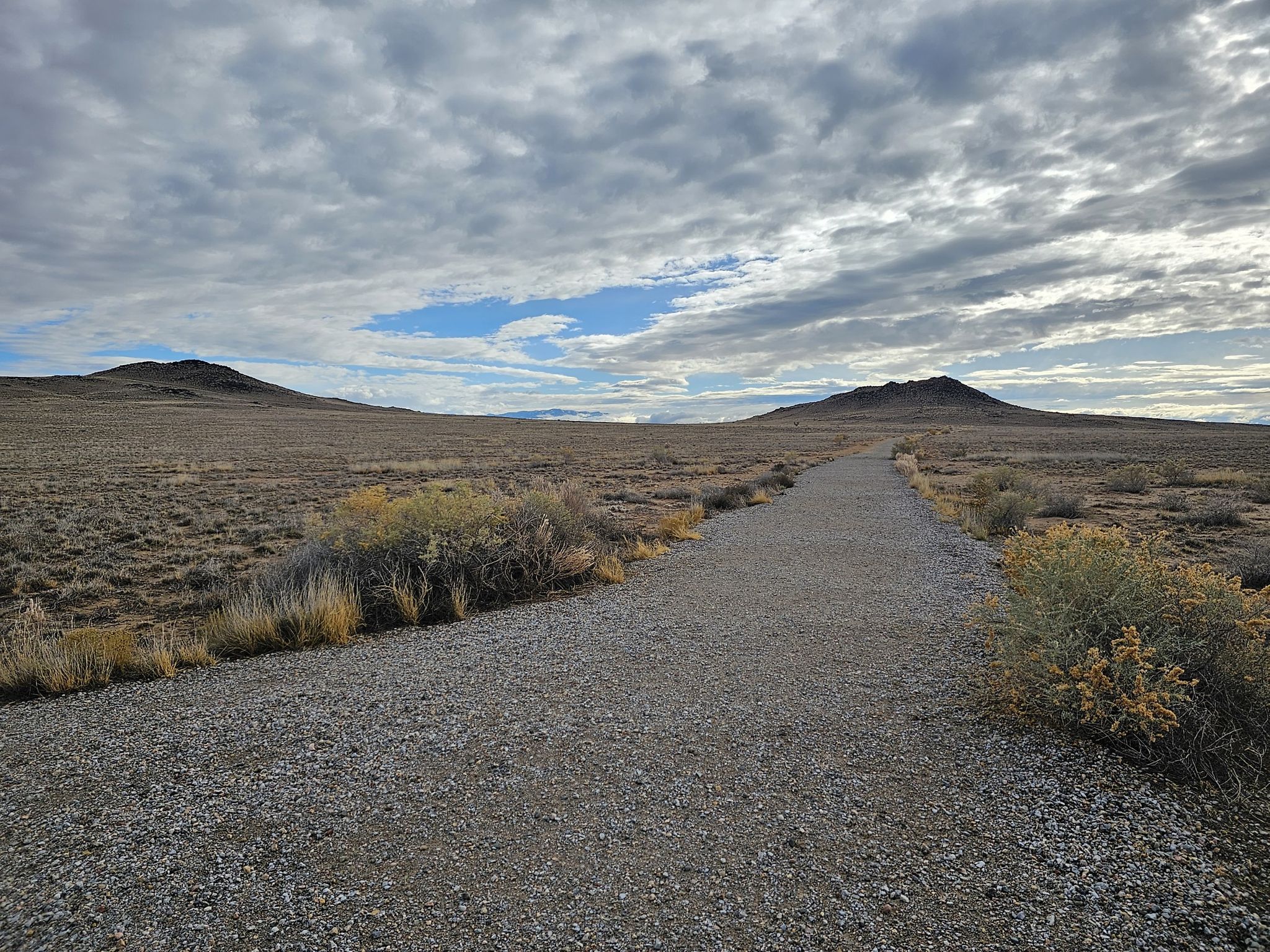 Gravel path through a wide, dry plain towards distant hills under cloudy sky. - Volcanoes Trail loop