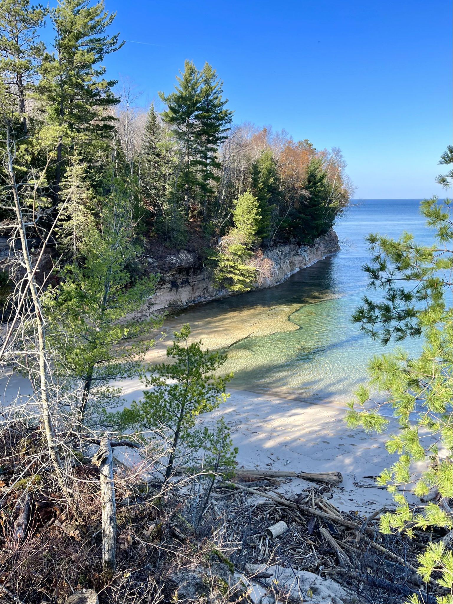 Clear water beach, rocky cliff, and evergreen trees under bright sun. - Little Beaver Lake to Chapel Rock Loop