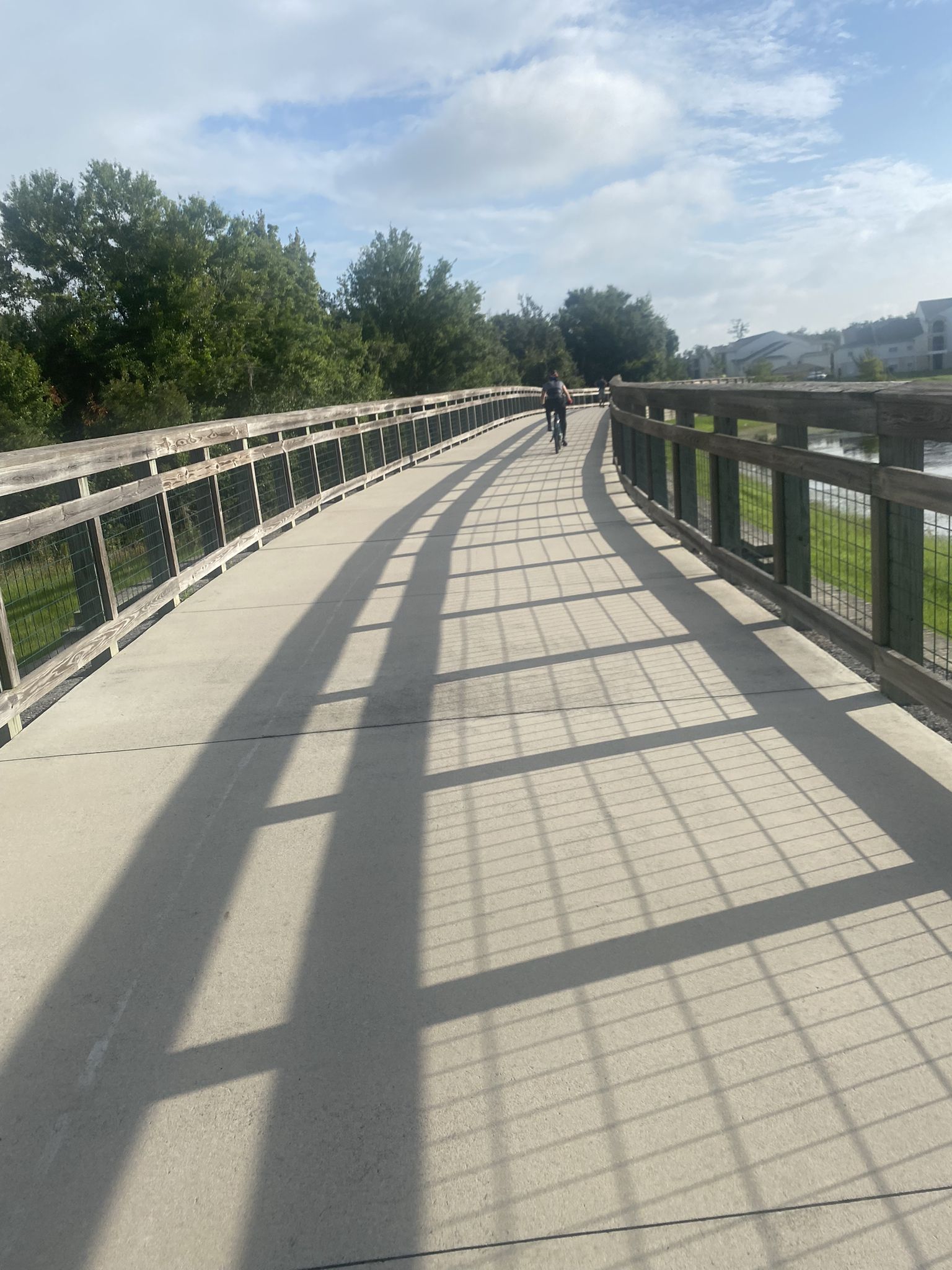 Person cycling on a long bridge with strong shadows on a sunny day. - Kissimmee Loop Trail