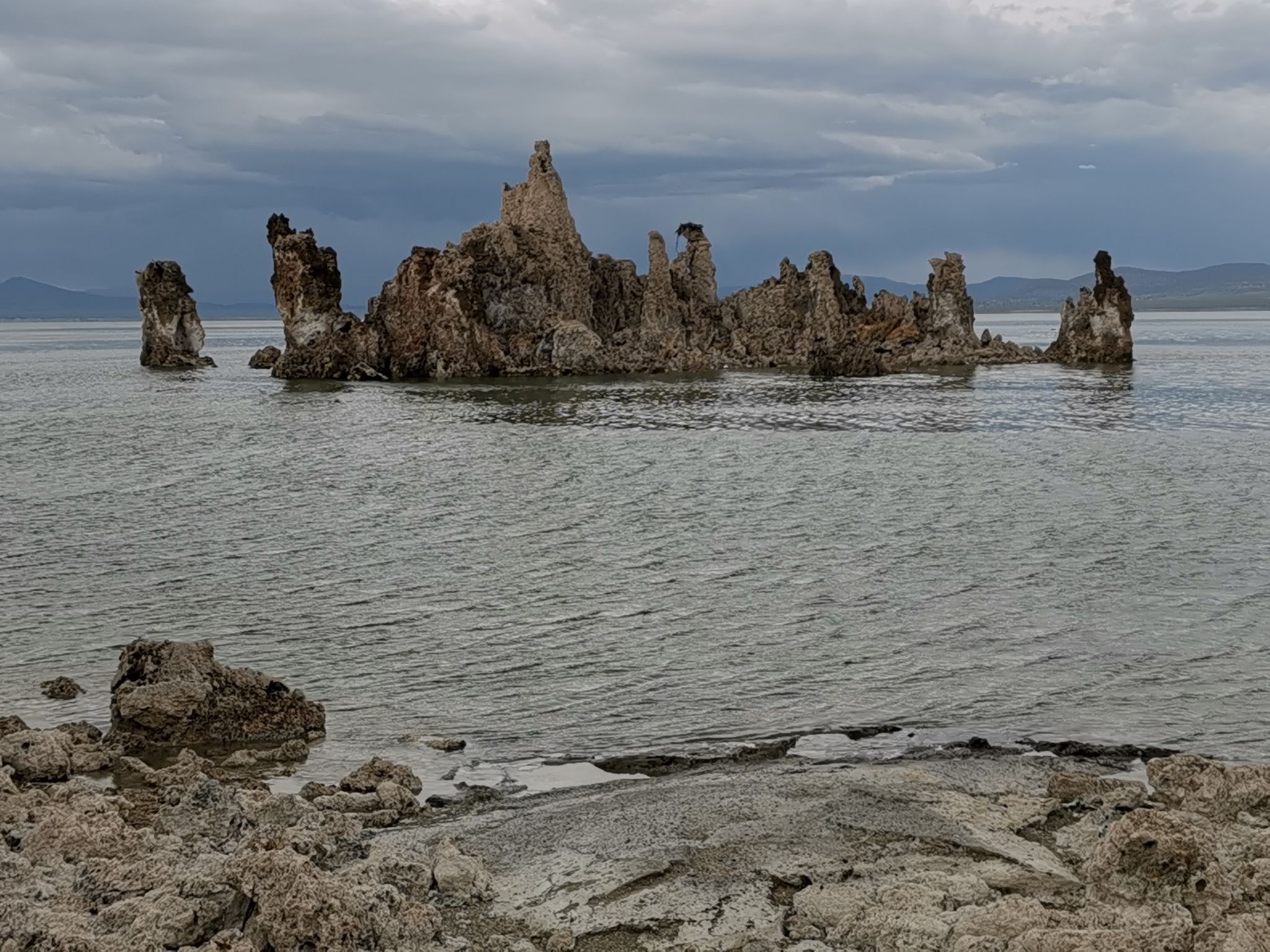 Tufa formations in a lake under a cloudy, overcast sky with rocky foreground. - South Tufa and Navy Beach Trail