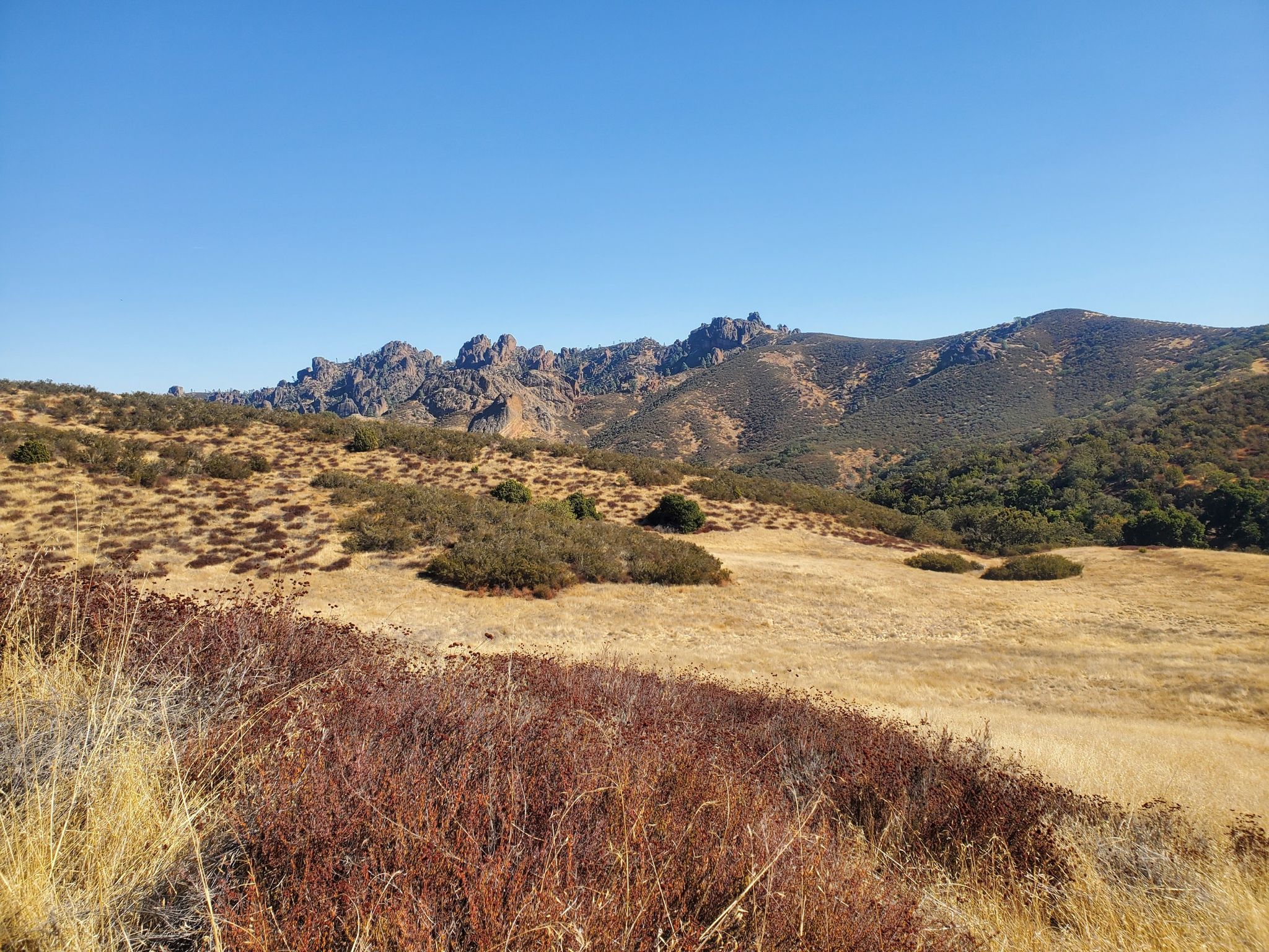 Rocky peaks overlook a dry, brush-covered landscape under a clear blue sky. - Prewett Point Trail