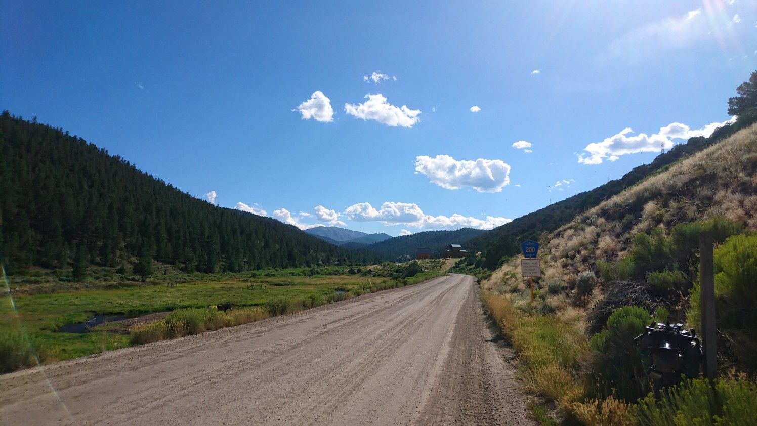 Long dirt road through a green valley with forested hills under a sunny sky. - Silver Creek - Rainbow Trail Loop