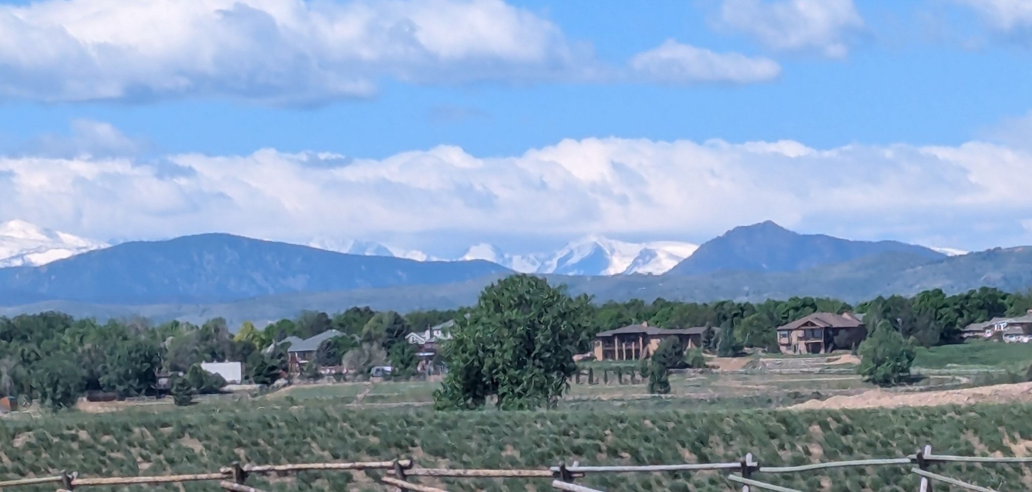 Distant snow-capped mountains under a bright sky, with houses and trees. - Arapaho Bend Natural Area loop