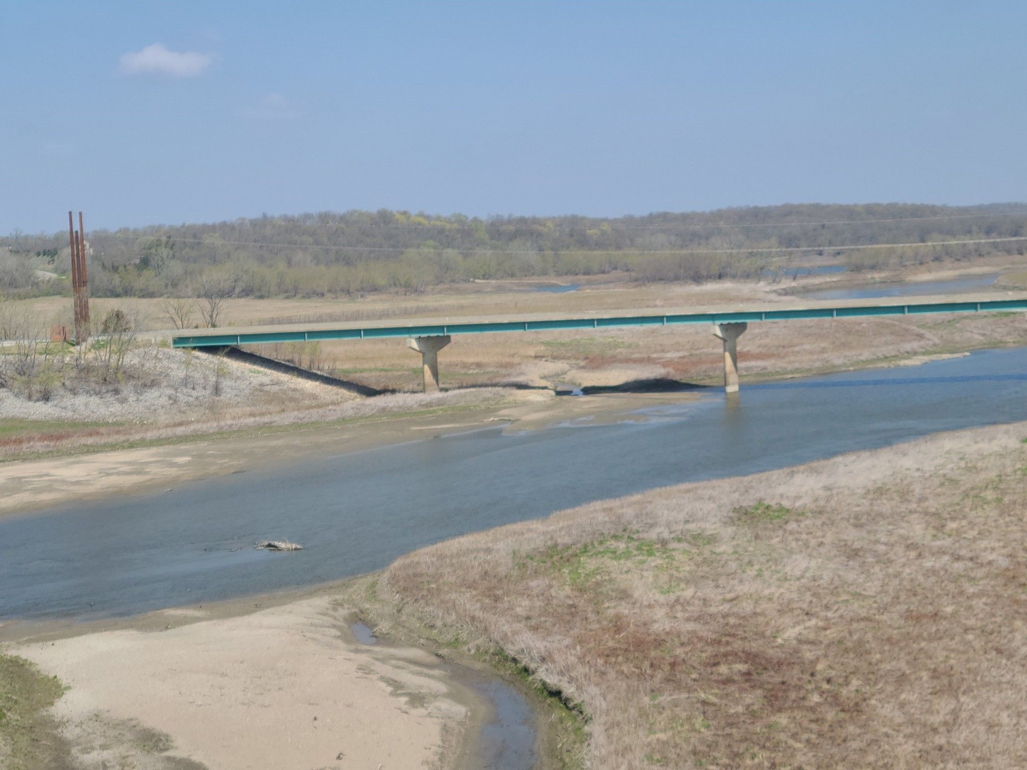 Long green bridge spans a wide river with dry banks on a clear day. - High Trestle Trail