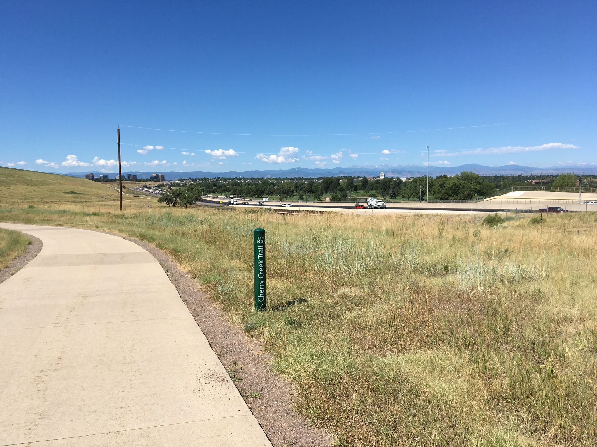 Paved trail curves through a grassy field with a green trail marker. - Cherry Creek Spur Trail loop from Arapahoe at Village Center