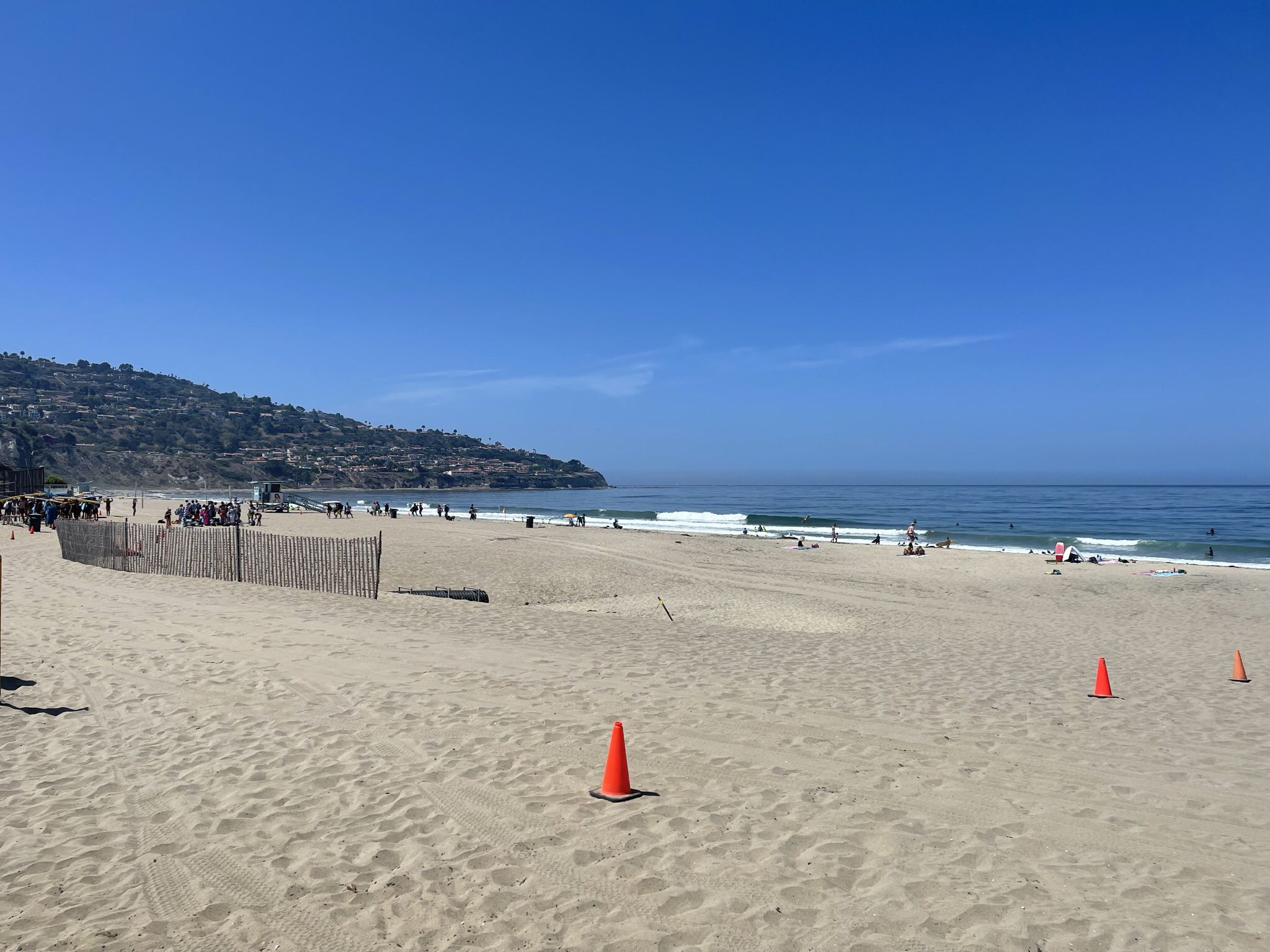 Sunny beach scene with orange cones, distant people, and calm ocean waves. - Ken Malloy Regional Park loop