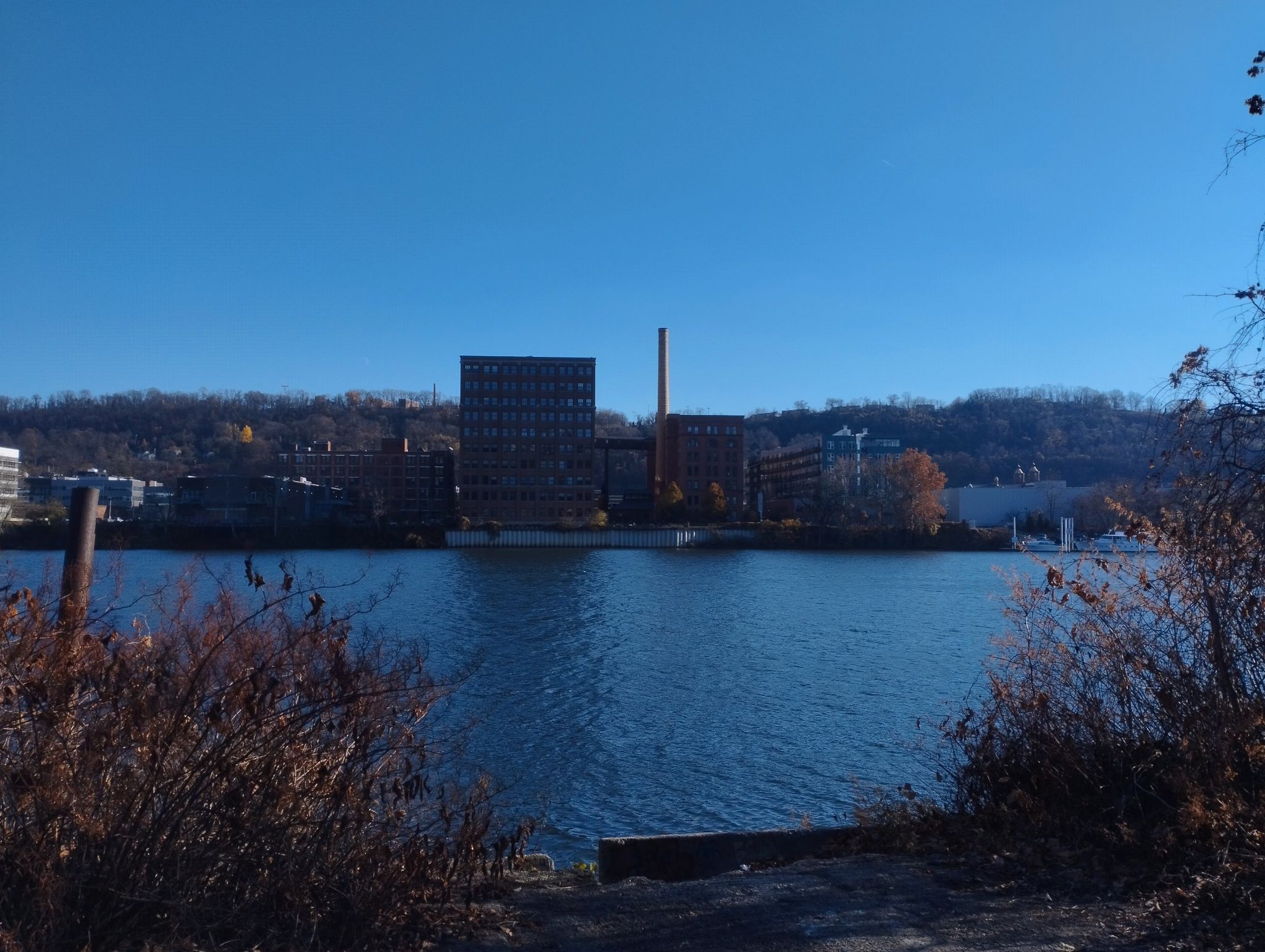 Industrial buildings and a smokestack across a wide river under clear blue sky. - North Shore Trail