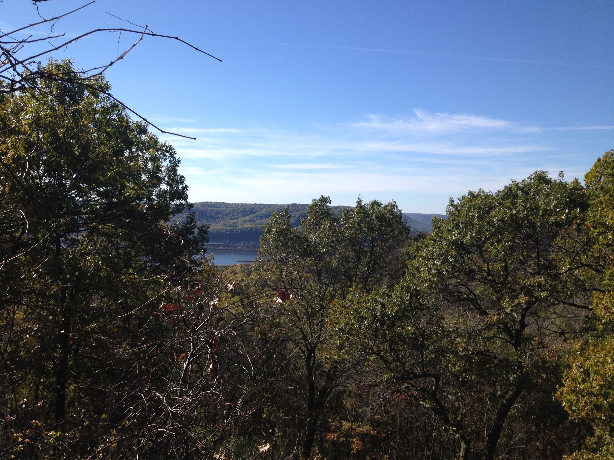 View through dark green trees to a distant river and hills under a blue sky. - Perrot Ridge – Reed's Peak loop from Perrot State Park