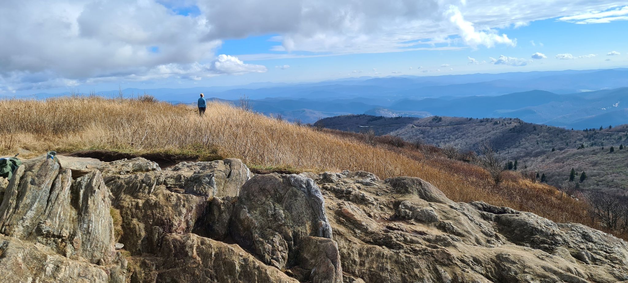 Person on a grassy hill overlooking mountains under a cloudy sky. - Black Balsam and Tennent Mountain Loop
