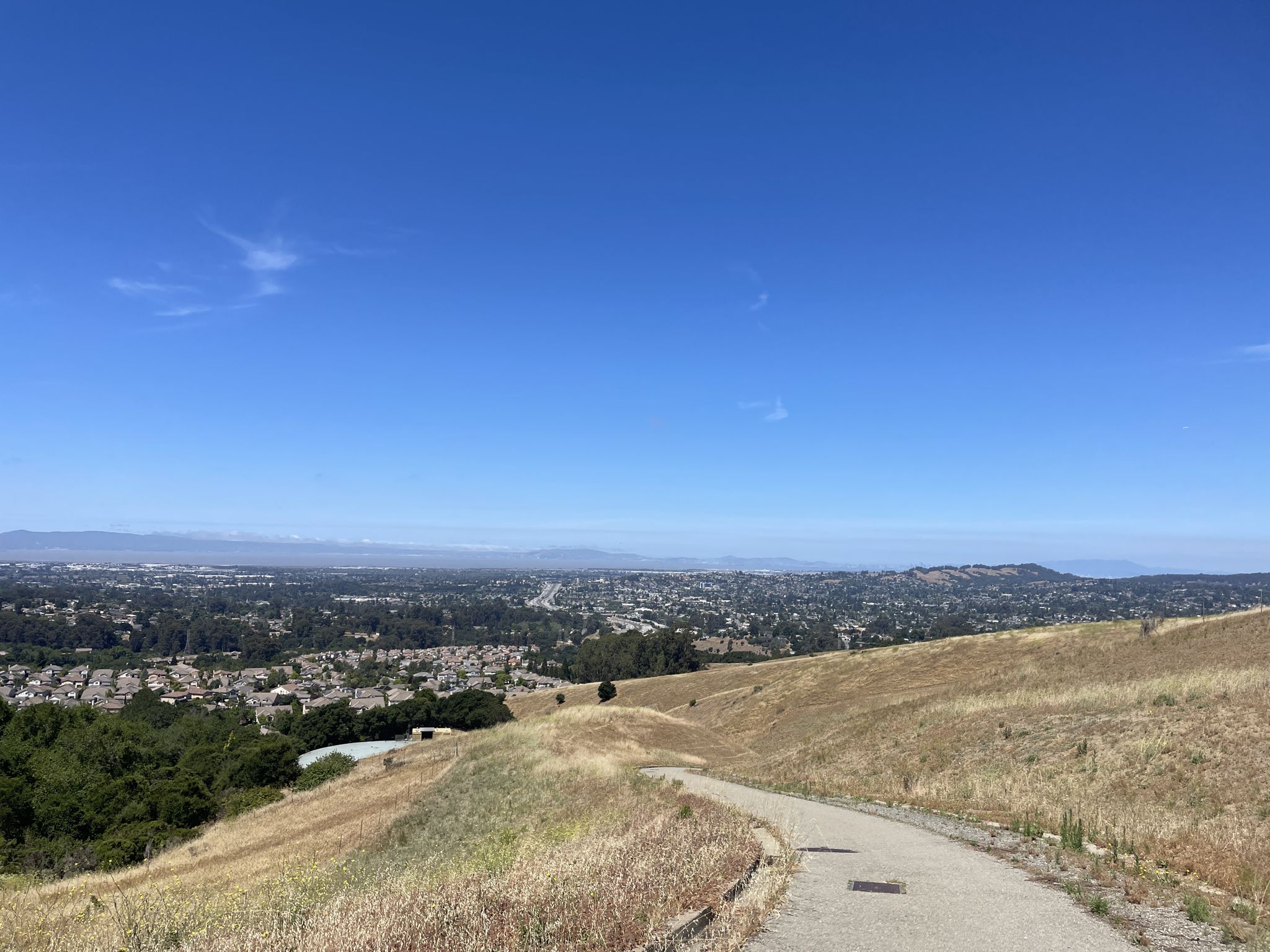 Paved path on a dry hillside with green trees and a distant city. - Independent School to Five Canyons and Newt Pond Trail