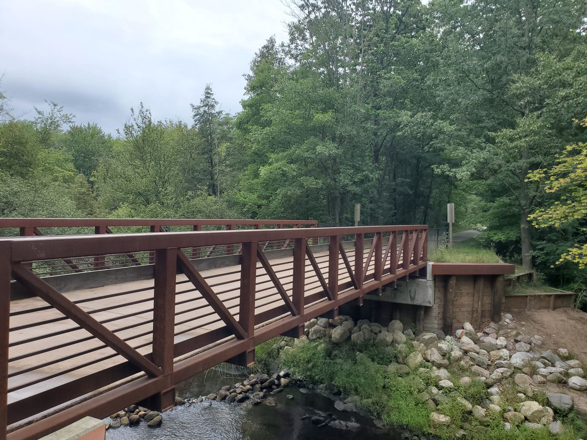 A sturdy wooden bridge spans a rocky stream, surrounded by dense green forest. - Treespeaker Woods loop from New Era