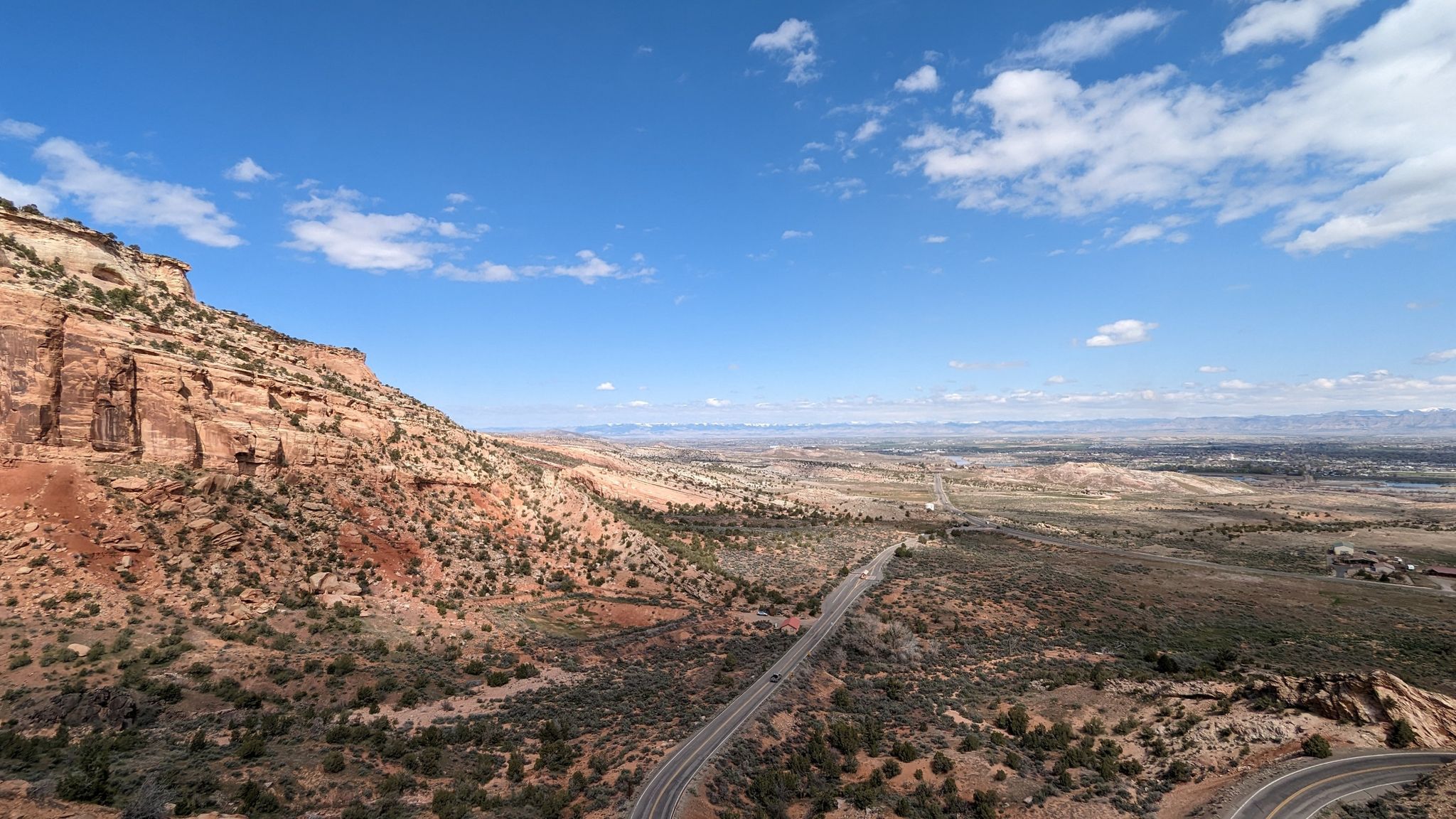 Winding road through a vast desert canyon under a bright blue sky. - Colorado National Monument Visitor Center via Rim Rock Drive