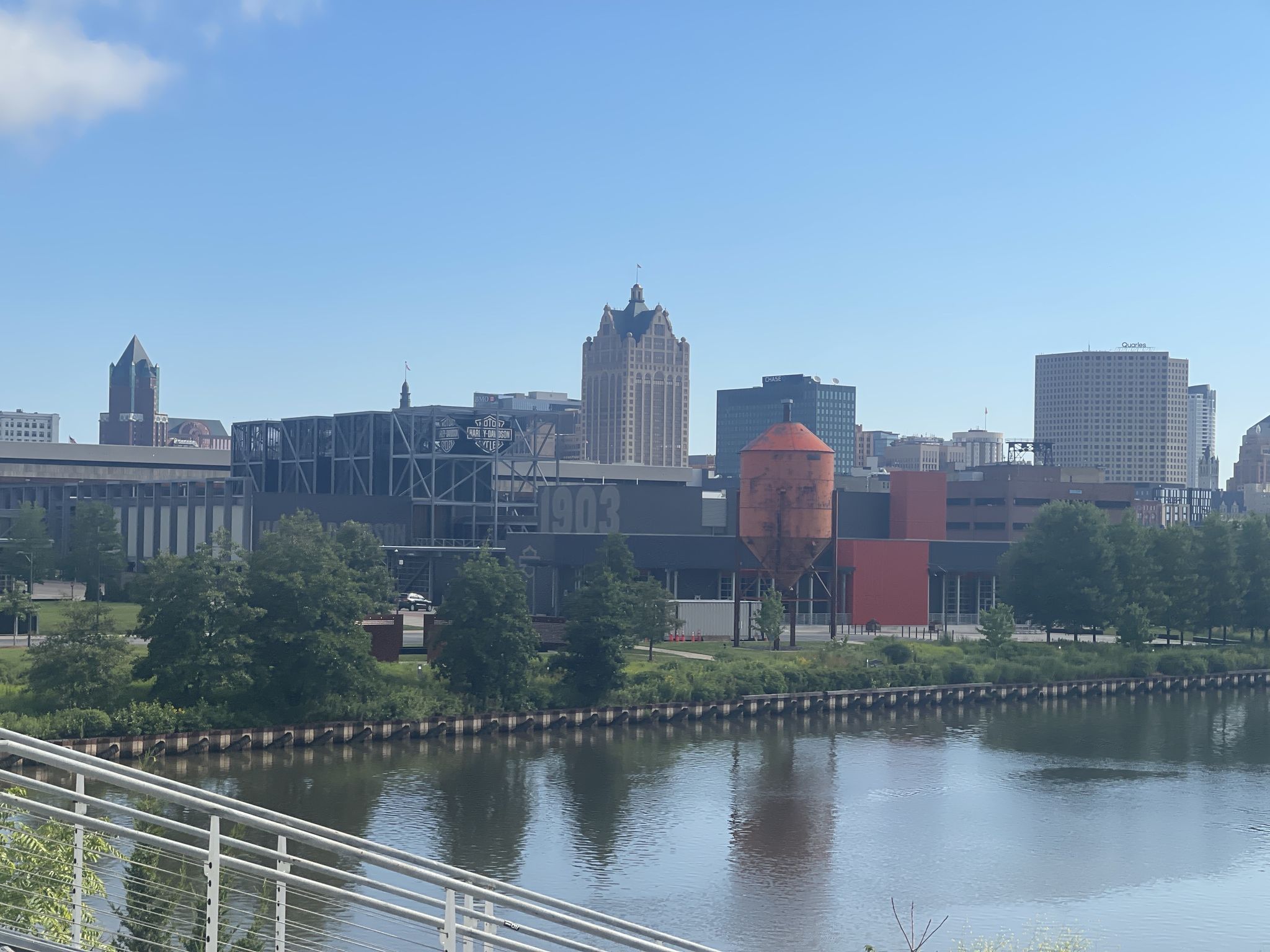 Sunny city skyline with a river and green trees reflecting in the water. - Hank Aaron State Trail