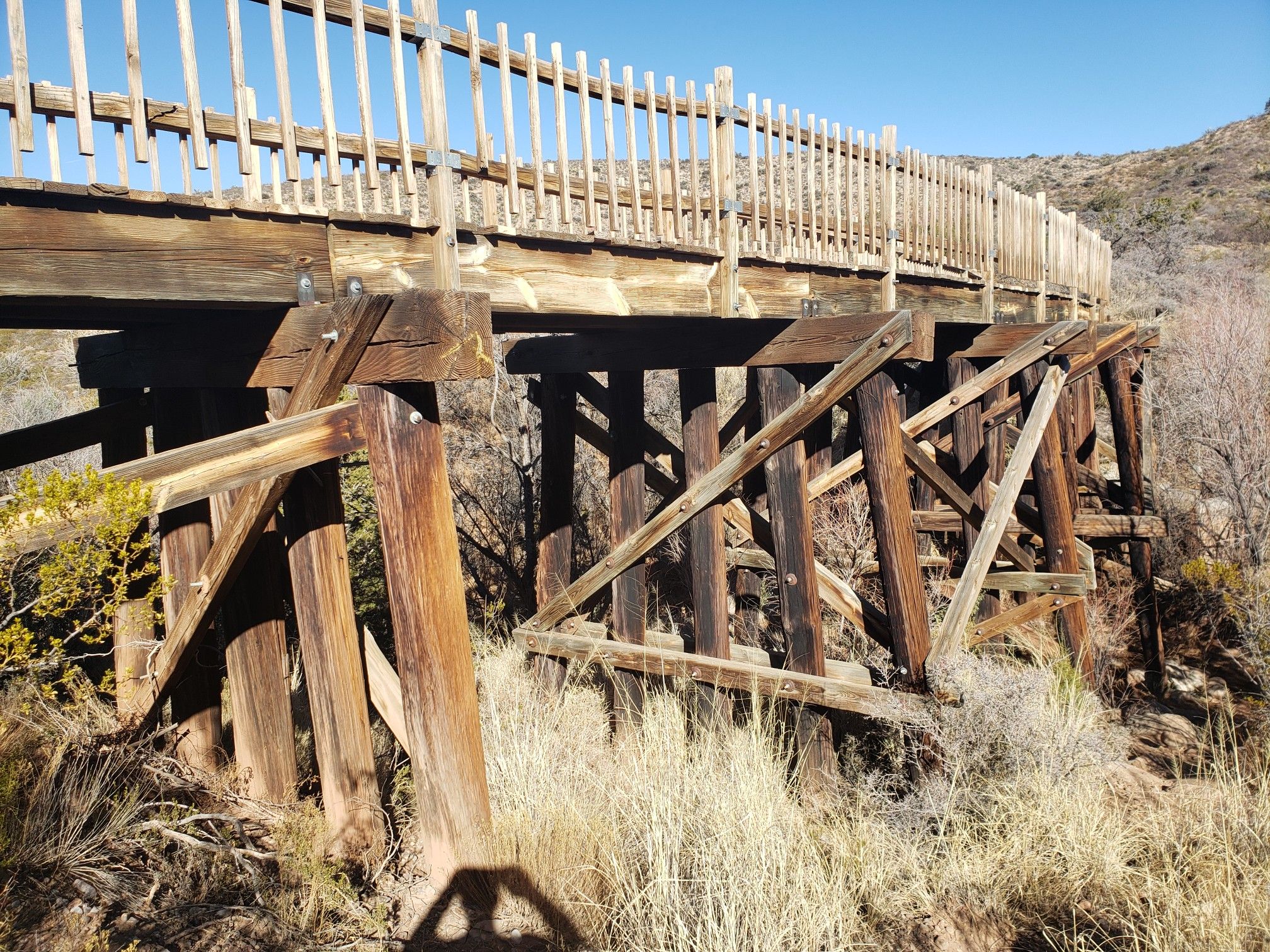 A sturdy wooden trestle bridge spans a dry, brushy landscape under a clear sky. - Bridal Veil Falls and Grand View Trail