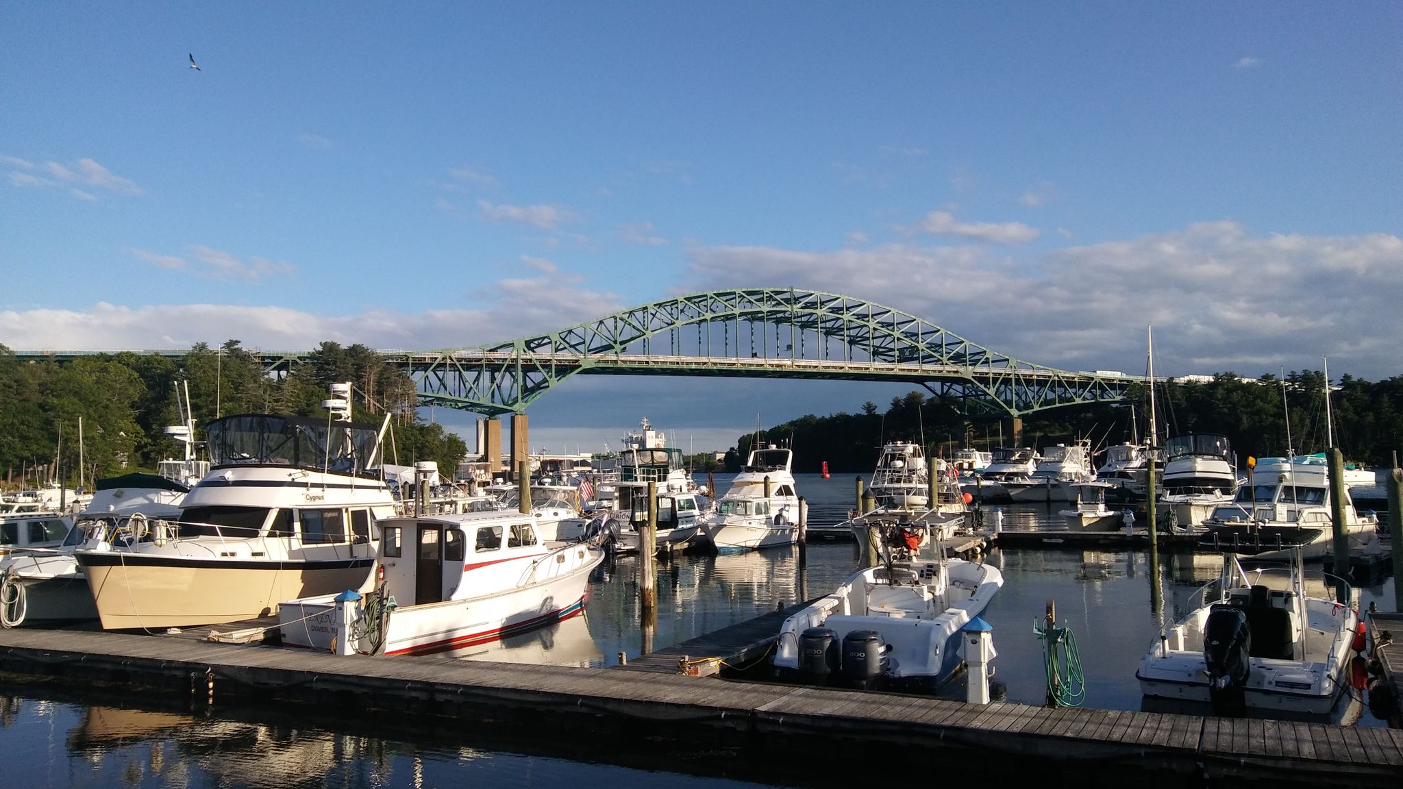 Marina with numerous boats docked, a large green arched bridge, under a clear sky. - Eliot Road via US Route 1 loop
