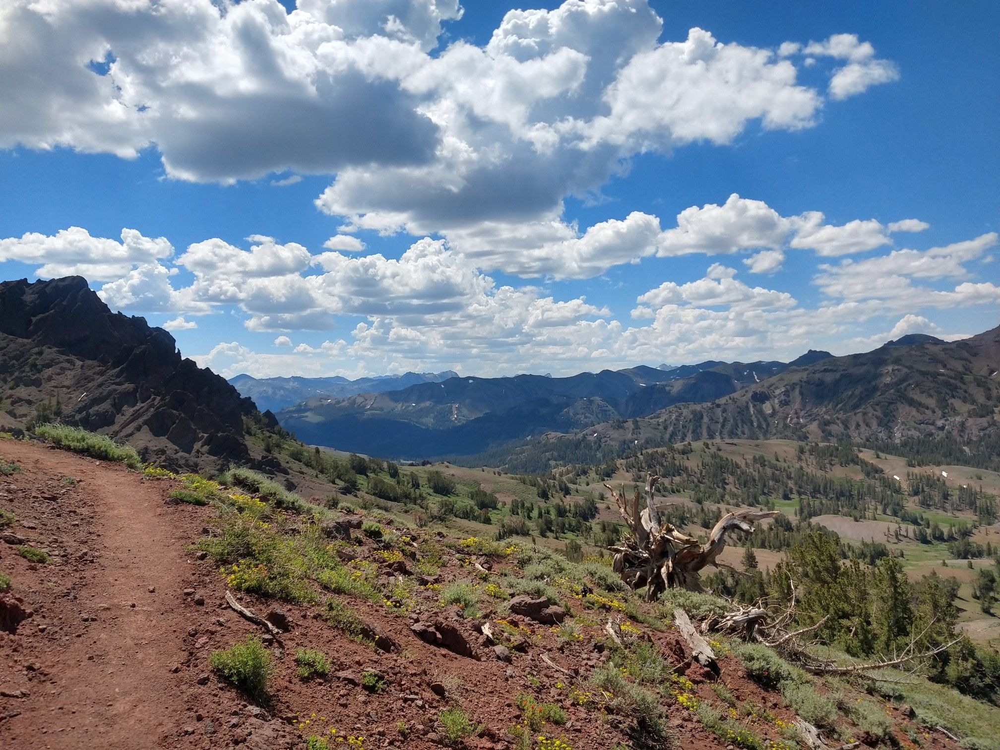 A winding dirt trail overlooks a vast, cloudy mountain landscape with valleys. - Sonora Peak Trail