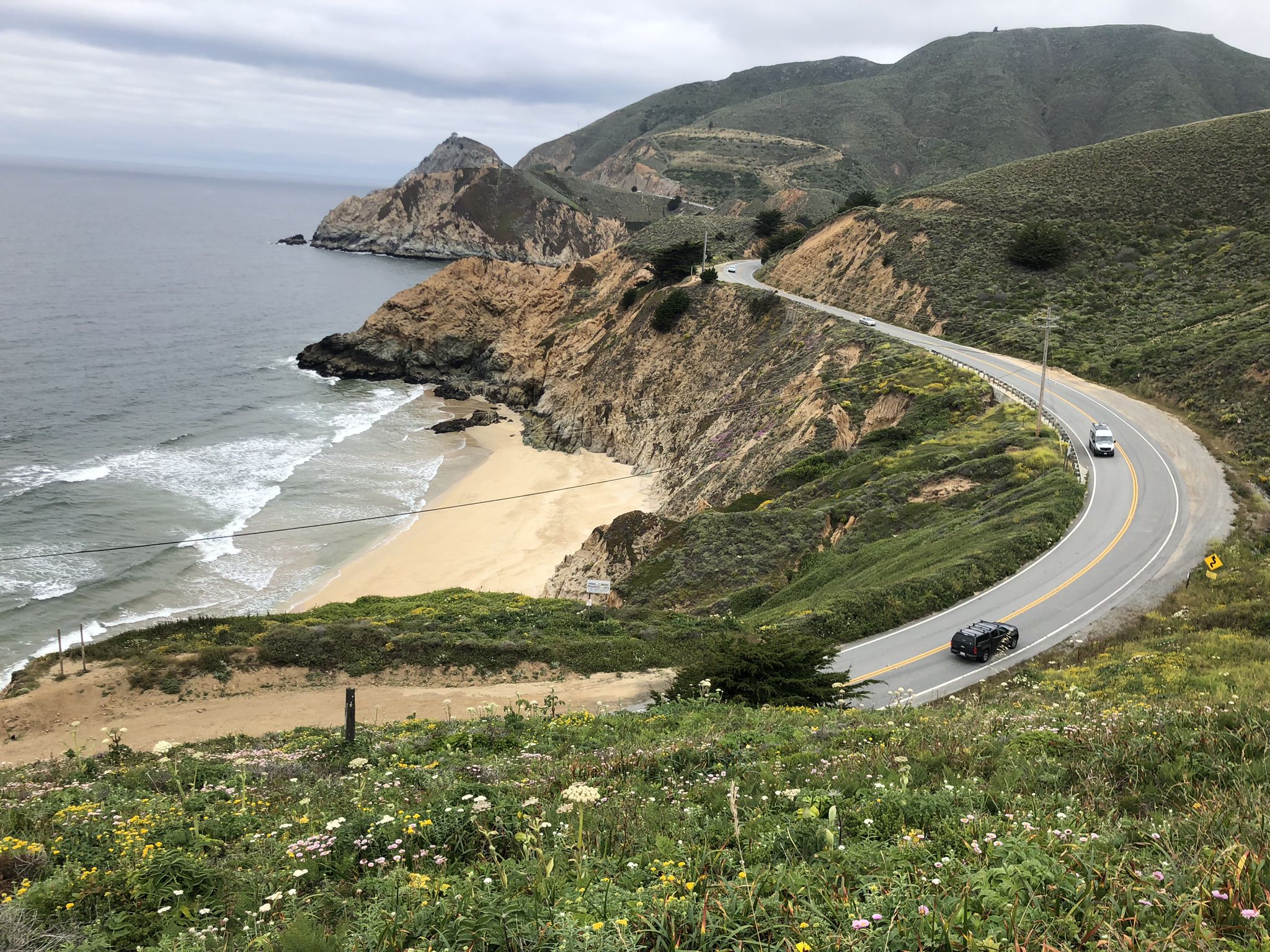 Winding coastal road with cars, a sandy beach, and green hills. - San Pedro Mountain to Old Colma Road Loop