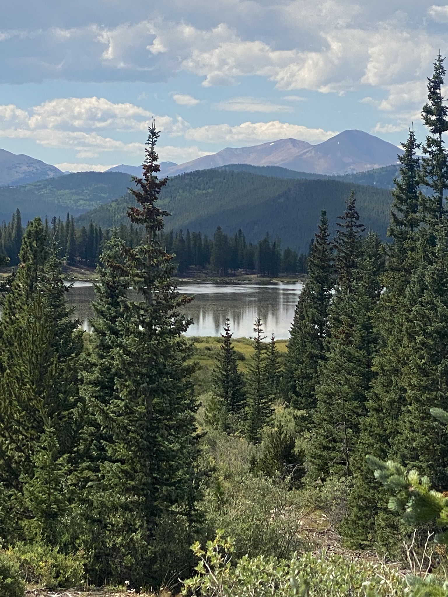 A serene lake surrounded by dense pine forests and distant mountains under a cloudy sky. - Echo Lake to Mount Blue Sky (Evans) Summit