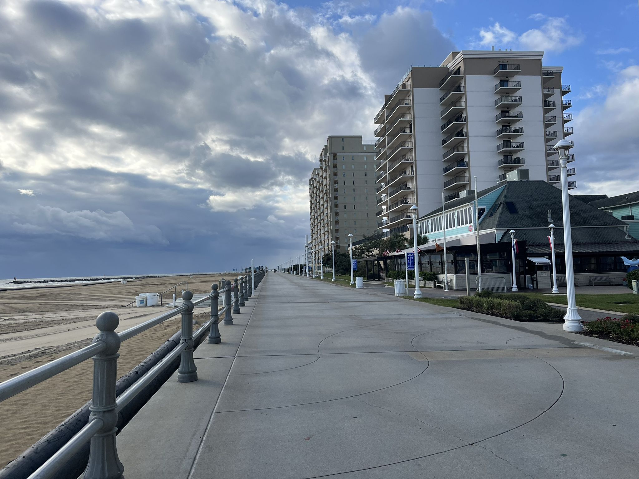 Boardwalk next to a sandy beach with tall buildings under a dramatic cloudy sky. - Fishing Pier – Virginia Beach loop from Virginia Beach