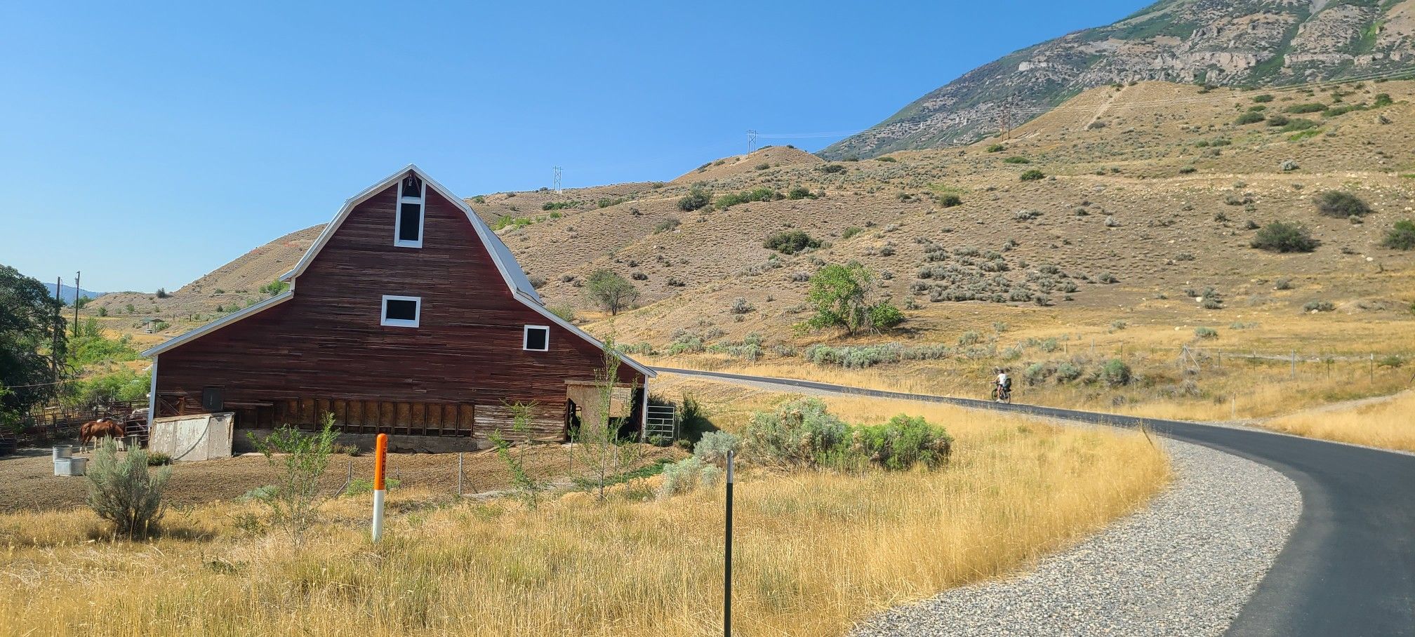 Red barn beside a paved path with a cyclist, backed by dry hills. - Murdock Canal Trail – Murdock Canal Trail loop from Cascade Professional Plaza