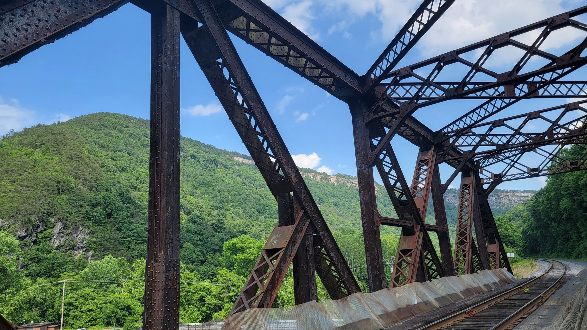 View through a rusty metal truss bridge towards green, forested mountains and tracks. - Roadbike loop from Cumberland