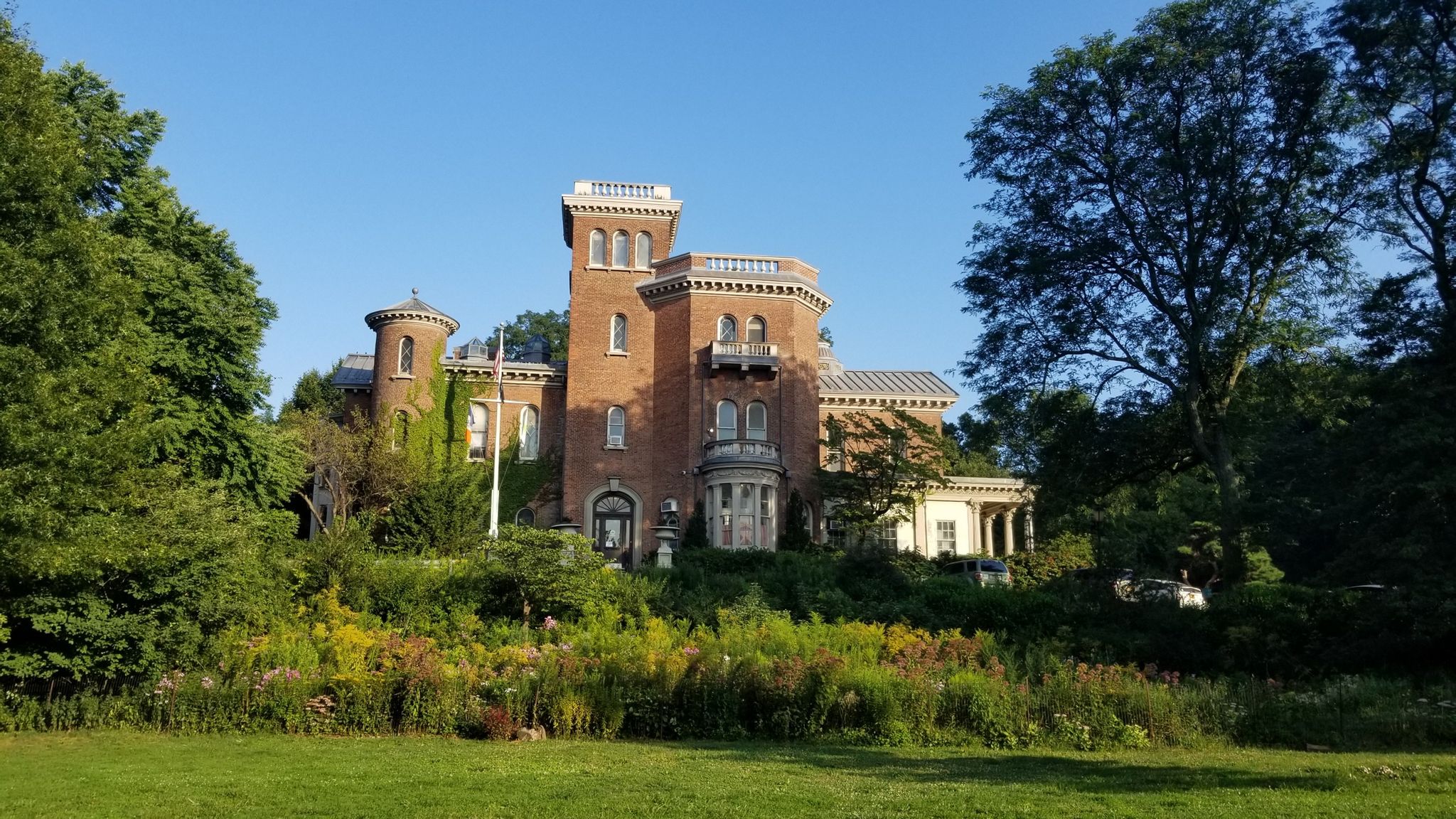 Ornate brick mansion surrounded by lush green trees and wildflowers, sunny day. - Peaks of Prospect Park