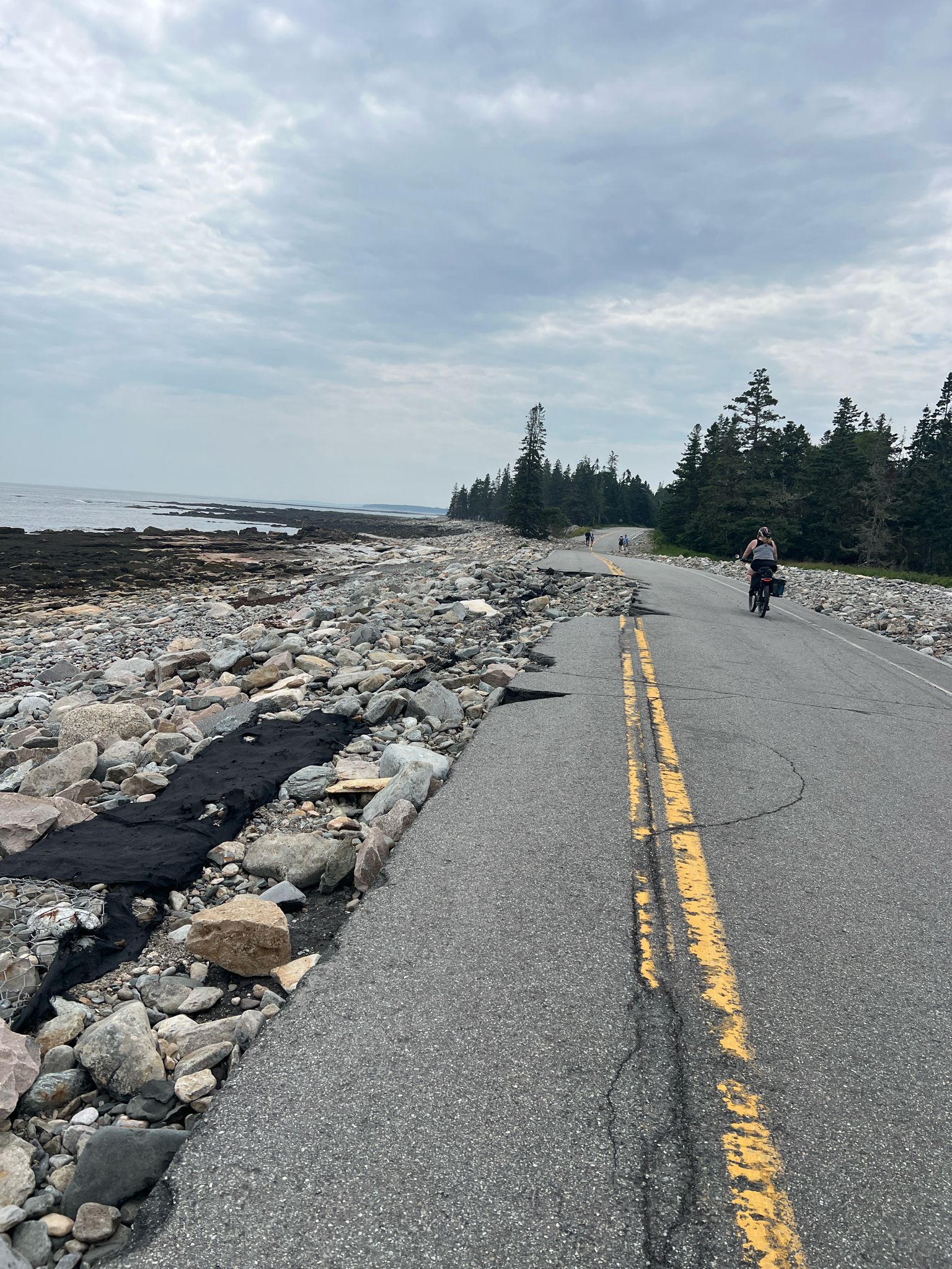 Person cycling on a damaged coastal road next to a rocky shore. - Bass Harbor Light Station & Seawall Road loop