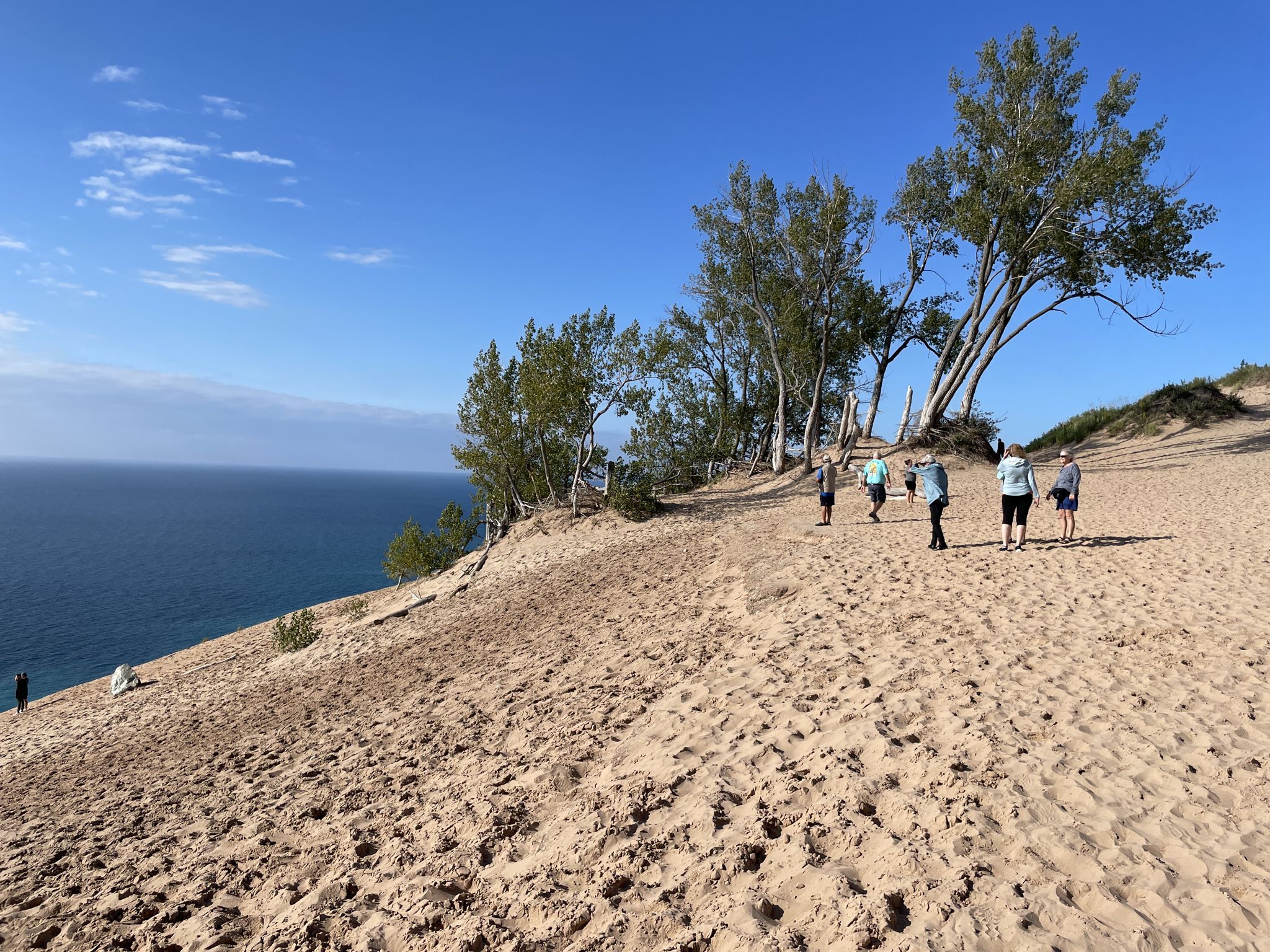 People walk along a sunny sandy dune overlooking a vast blue lake. - Pierce Stocking Scenic Drive