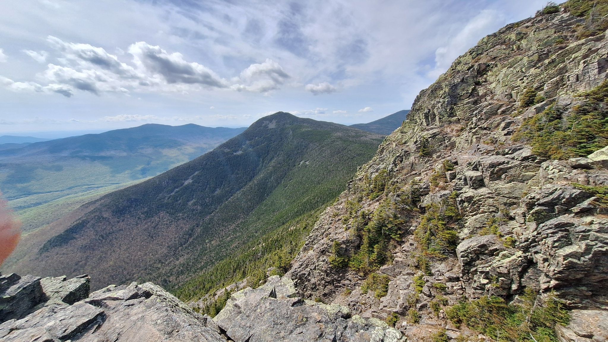 Steep rocky mountain slope with distant forested peaks under a partly cloudy sky. - Old Osseo Trail to Mount Flume