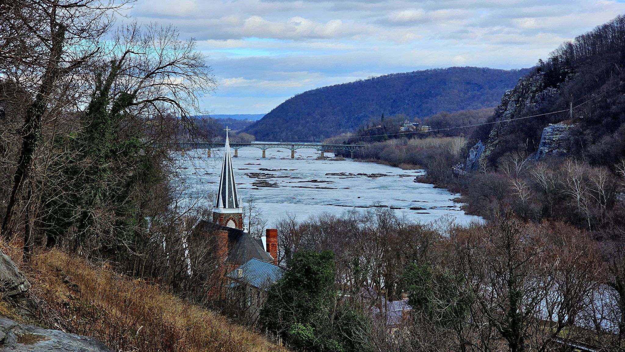 Overcast view of a wide river valley with a church steeple and distant bridge. - Jefferson Rock – John Brown's Fort loop from Harpers Ferry