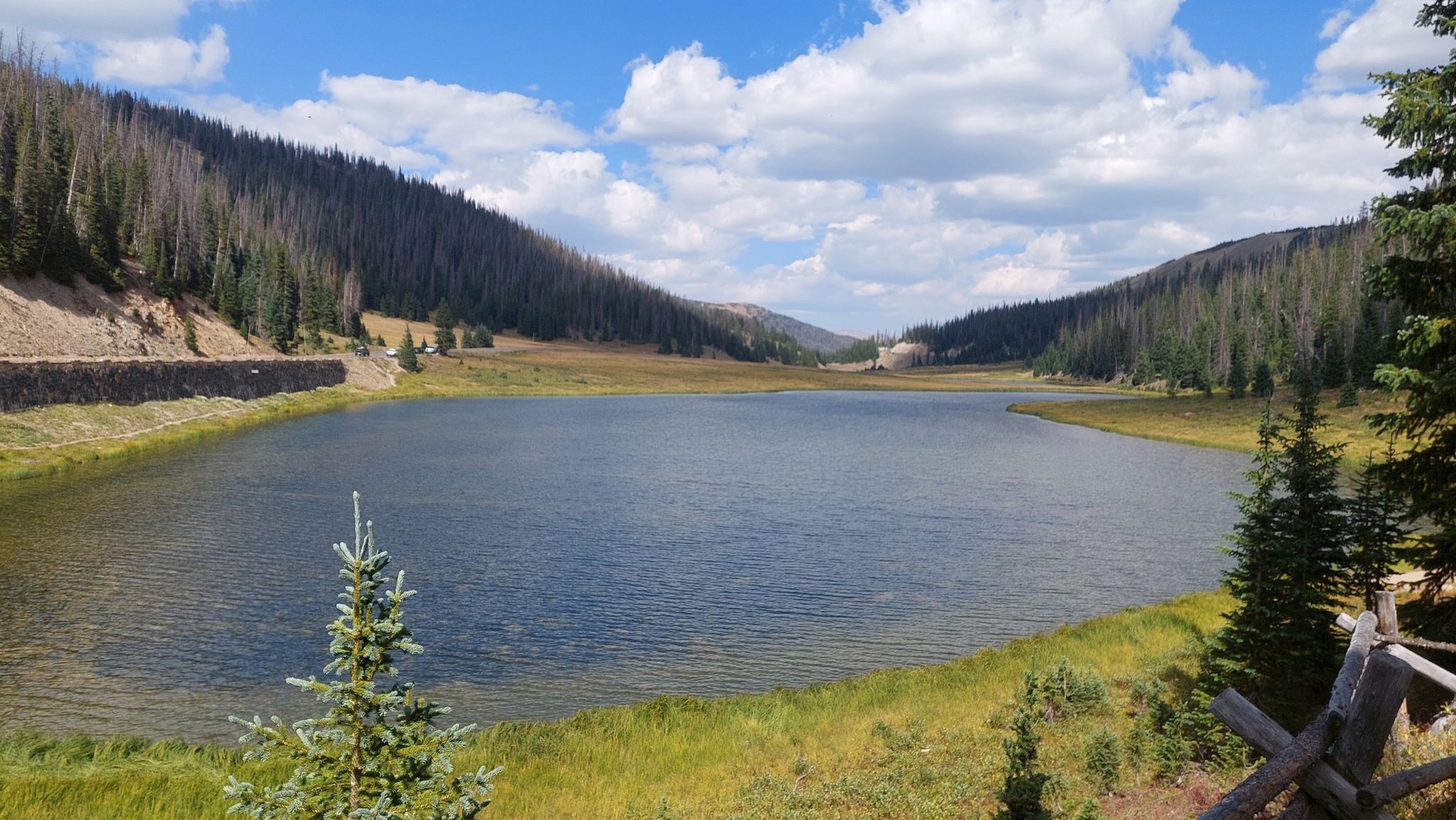 Sunny lake nestled between forested hills, with a bright blue sky. - Mount Ida Trail