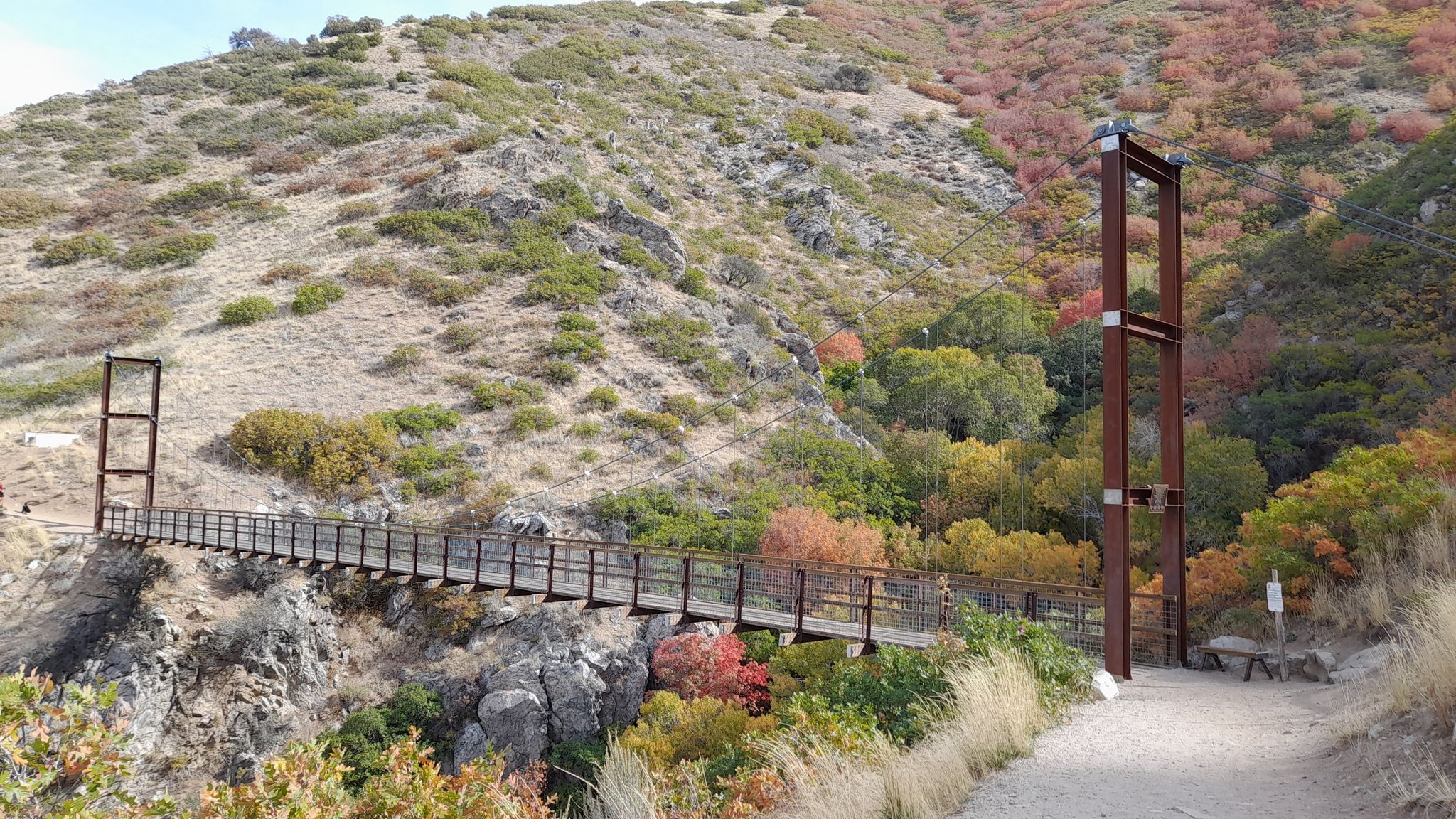 Suspension bridge over a ravine, surrounded by hills with autumn foliage and dry brush. - Bear Canyon Bridge via Bonneville Shoreline Trail